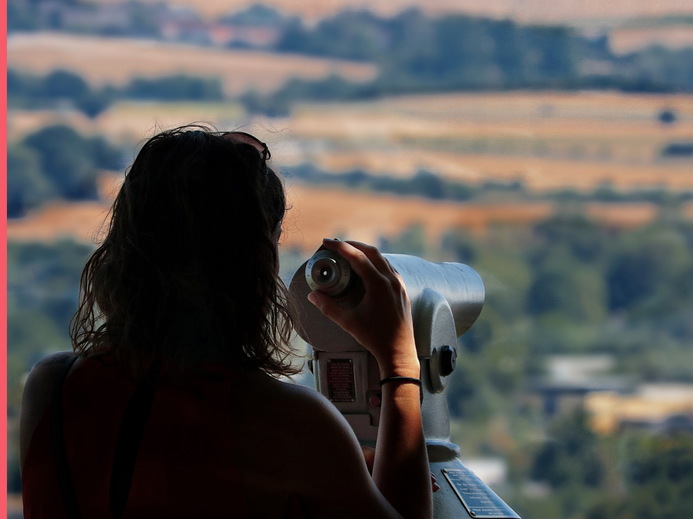 Woman using telescope to view landscape in the distance.