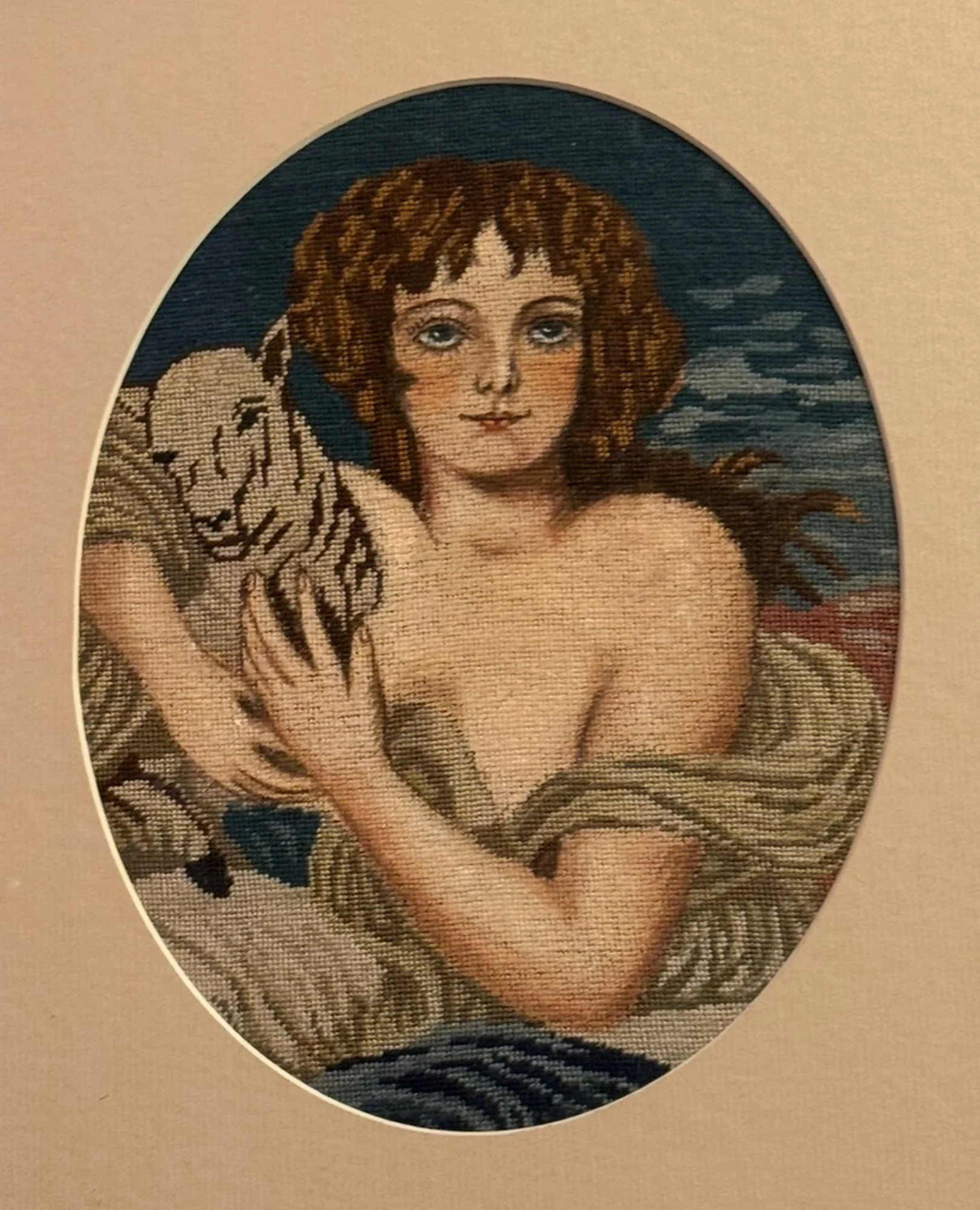 Cross-stitch art of a woman with curly brown hair, blue eyes, and a white animal, possibly a cat, resting on her shoulder, with a dark sky background