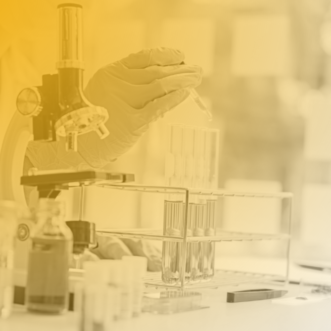 Laboratory technician wearing gloves handles test tubes in a lab setting with scientific equipment.