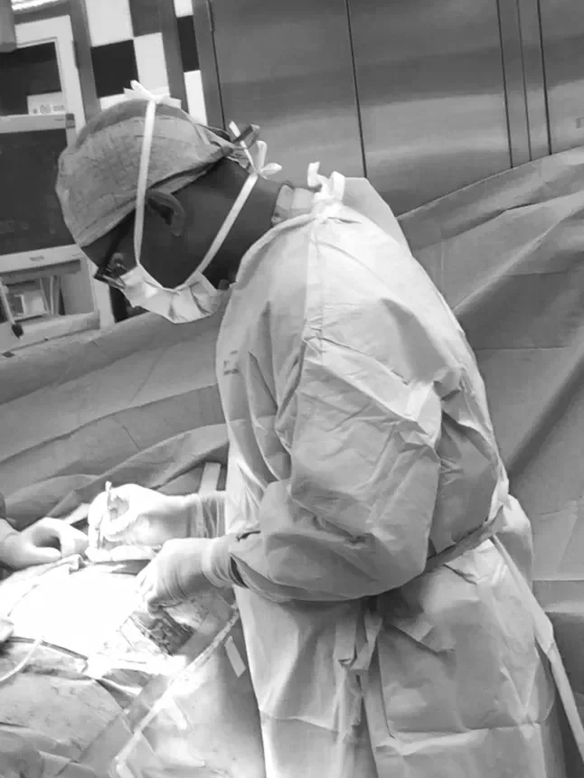 Medical professional wearing protective gear performing surgery in an operating room.
