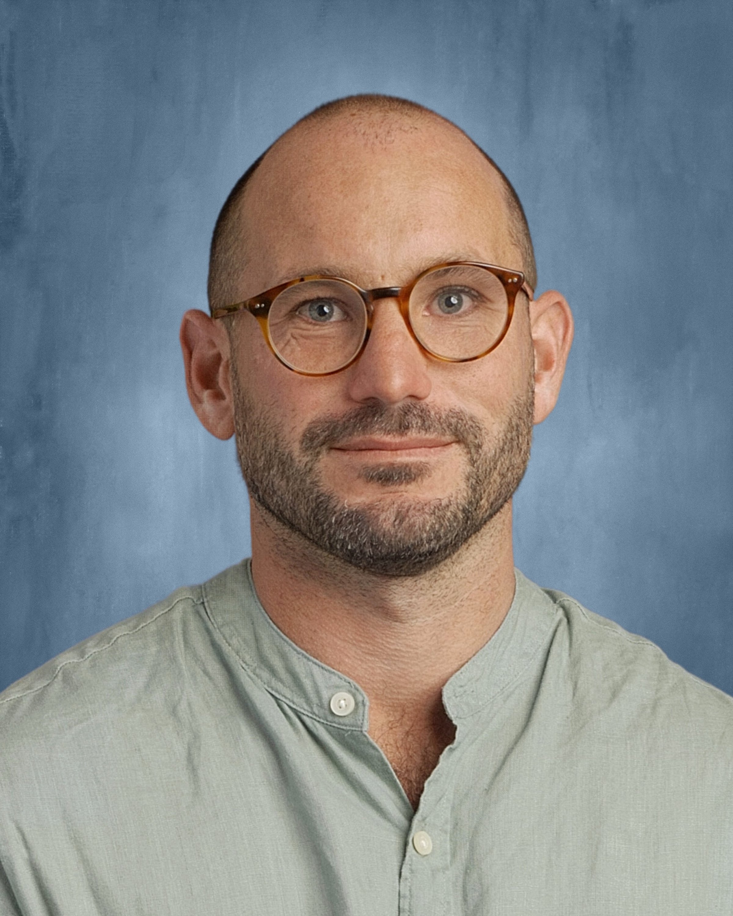 Close-up of a man with a beard and glasses, wearing a light green button-up shirt, against a blue background.