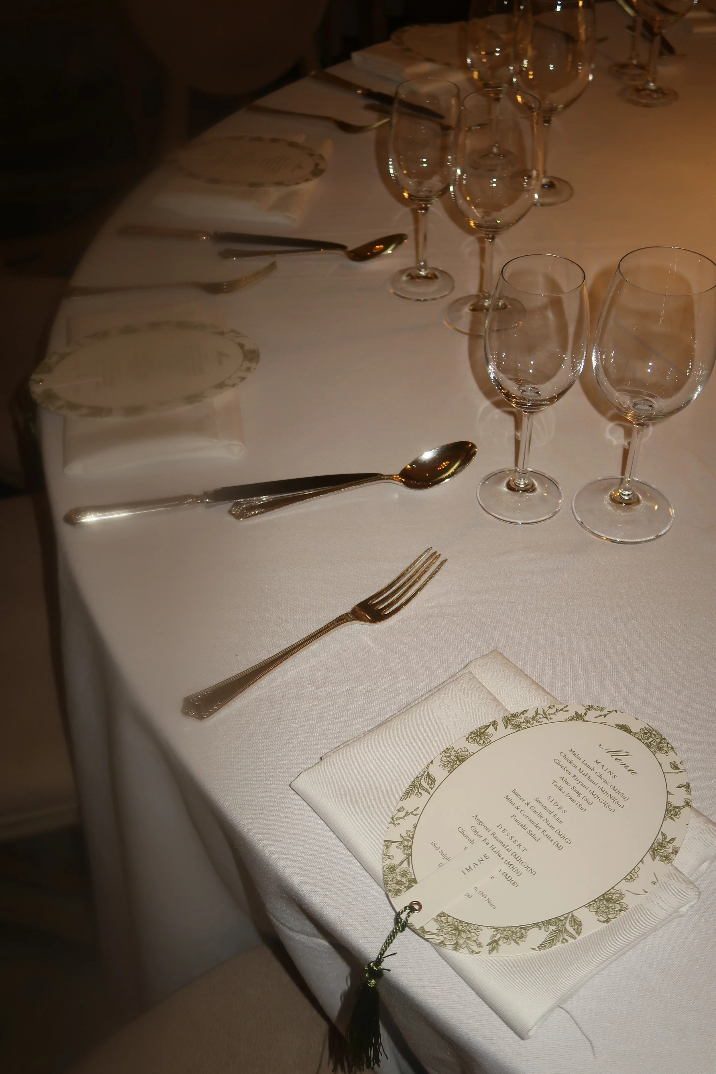 Elegant dining table set with four empty wine glasses, silverware, and a menu on a white tablecloth, in a dimly lit restaurant setting.