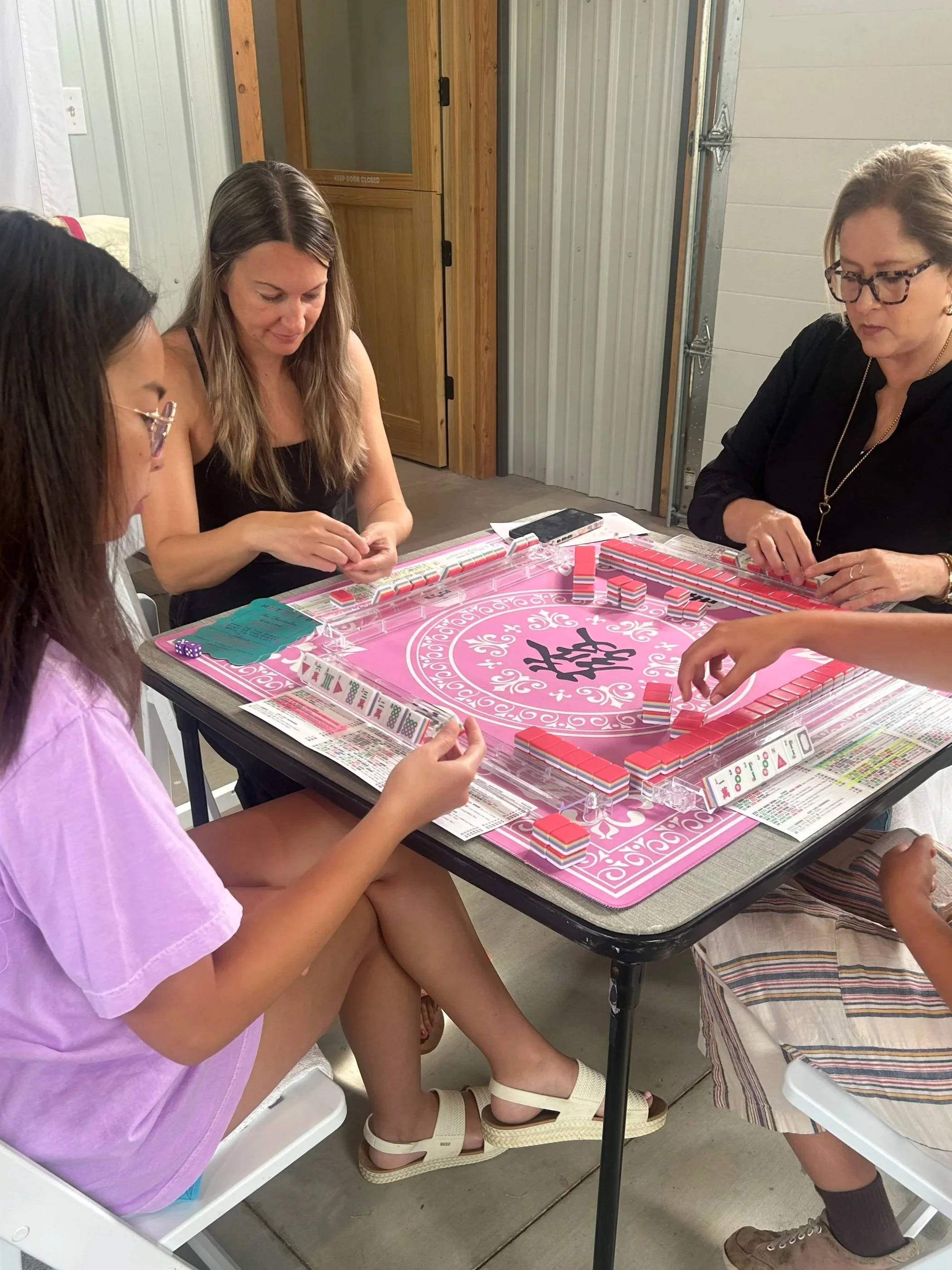 People playing a game of Mahjong at a table in a garage or workshop space.
