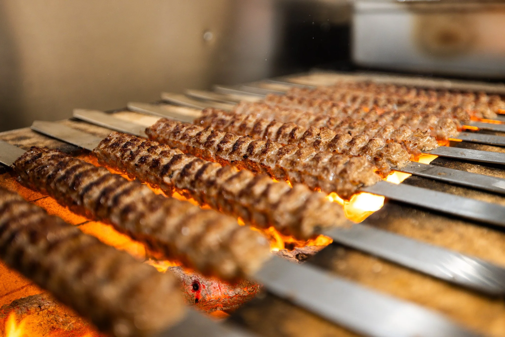 Close-up of skewers of seasoned ground beef grilling over open flames on a barbecue grill.