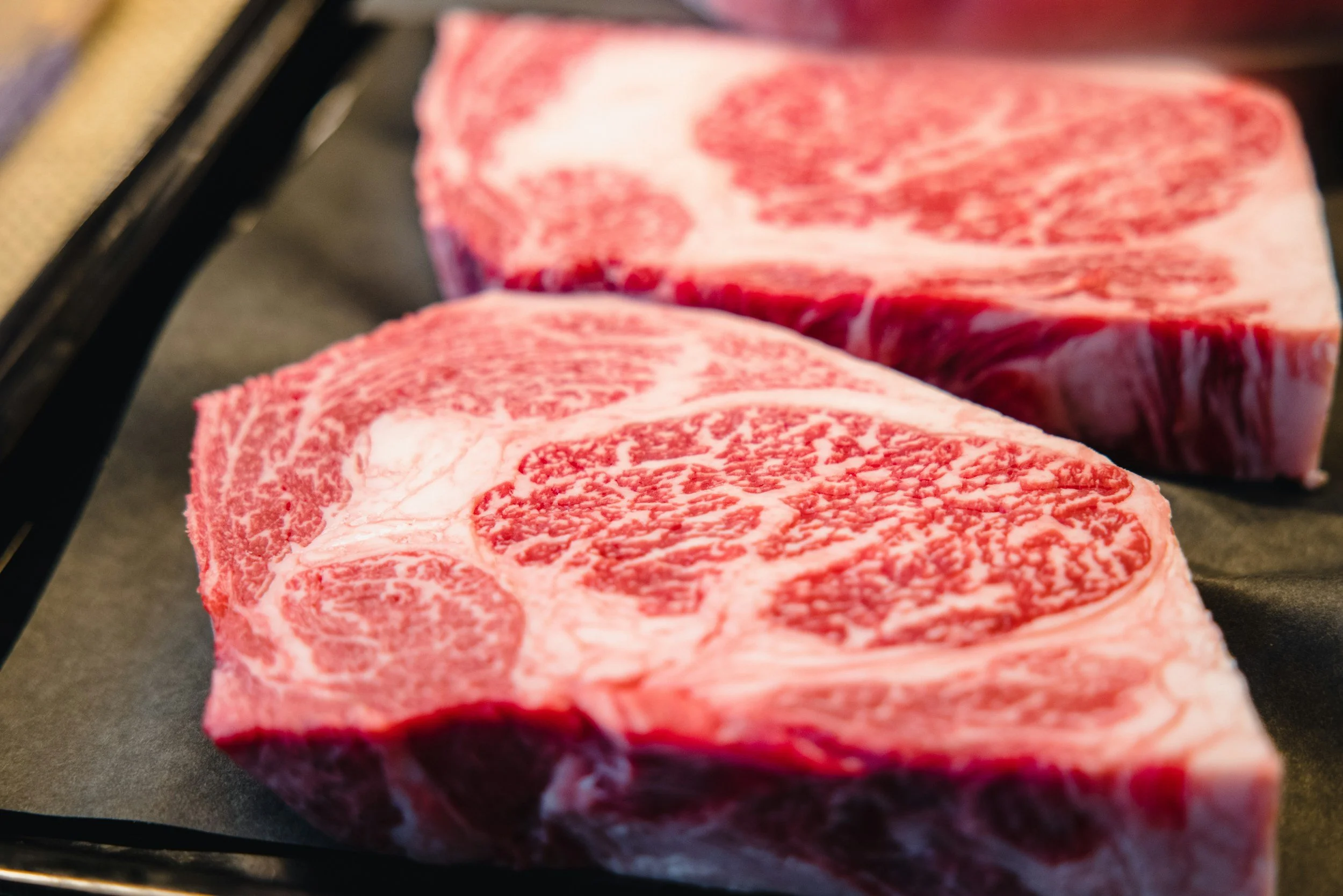 Close-up of three raw beef steaks with marbling on a black surface.