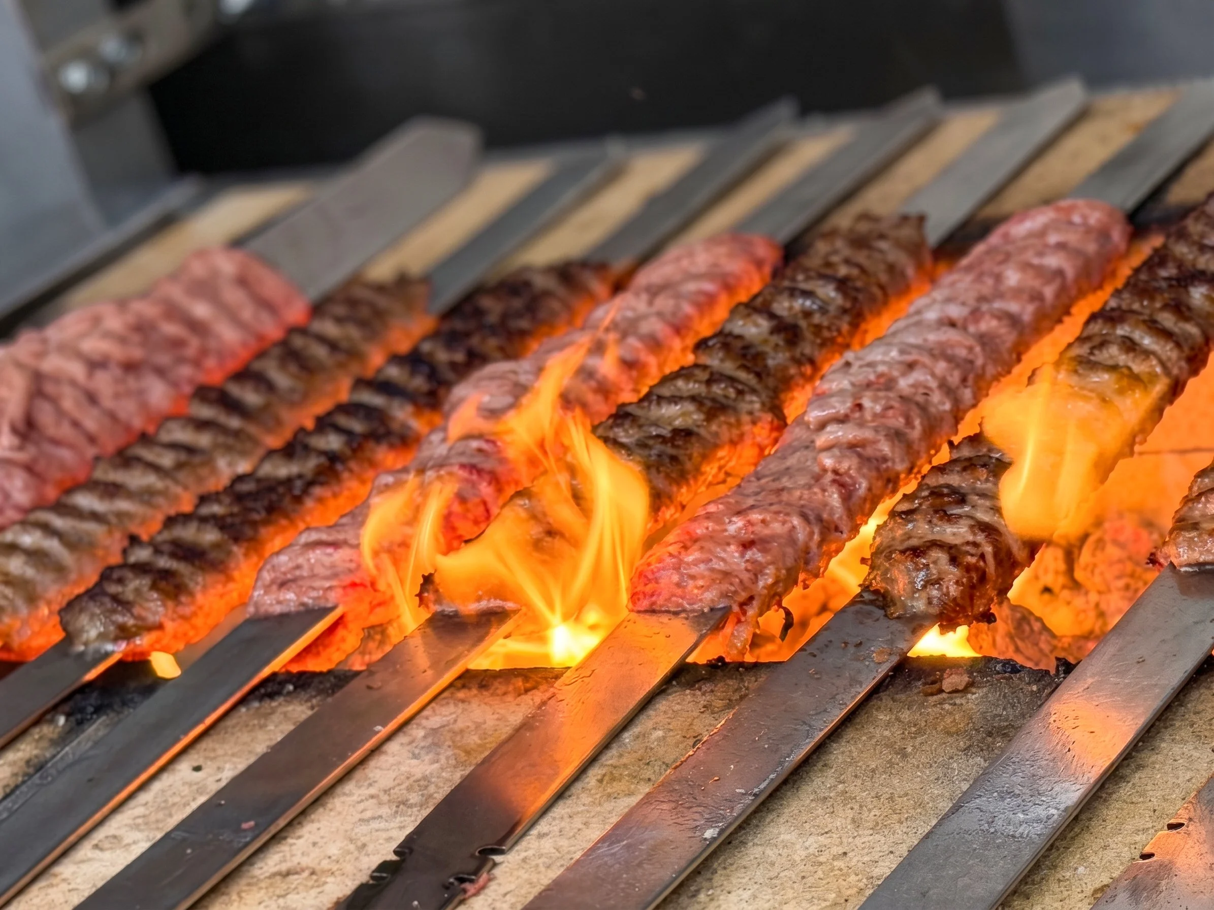 Close-up of beef and lamb kebabs grilling over open flames on a barbecue grill.