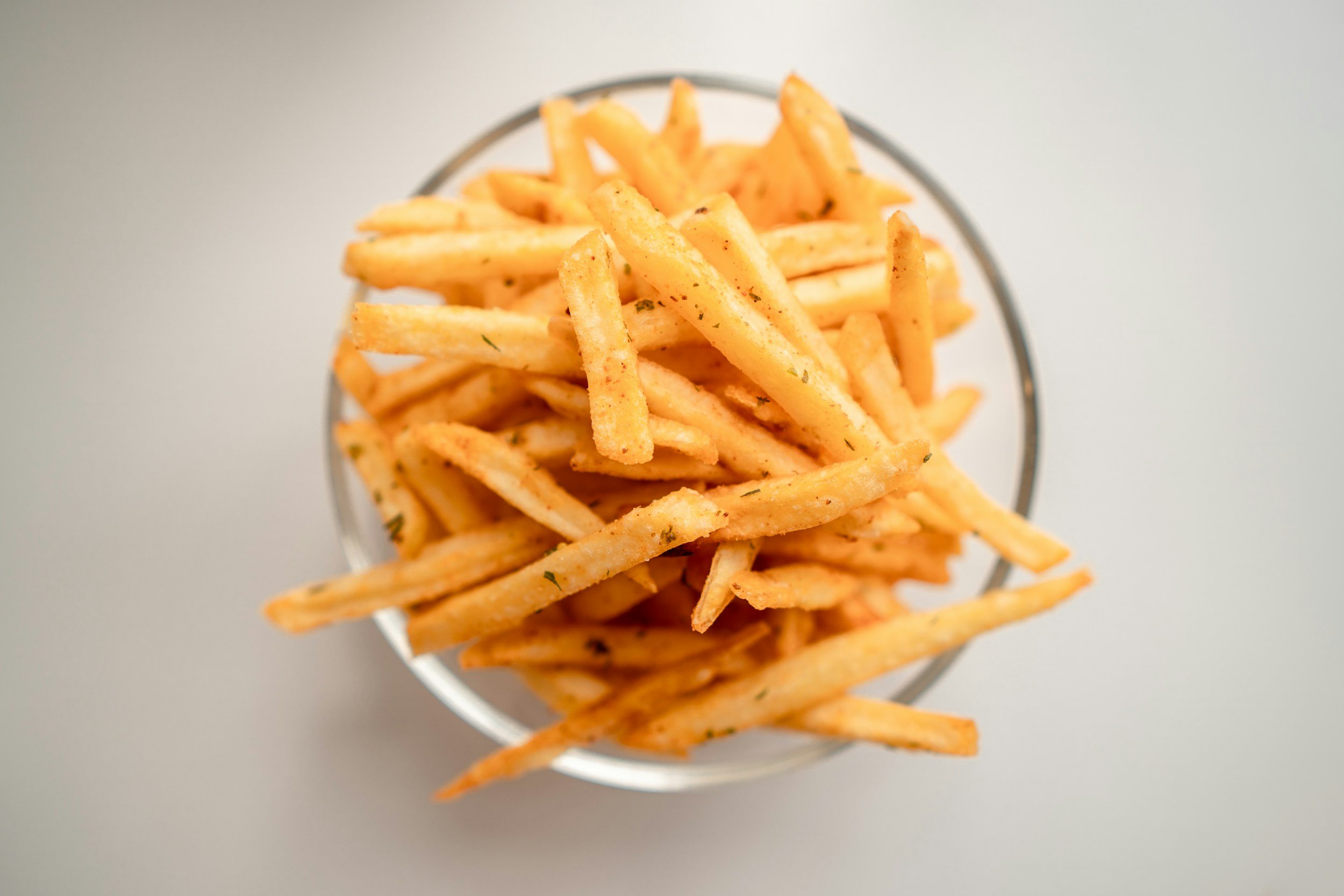 French fries in a metal basket topped with herbs on a white background.