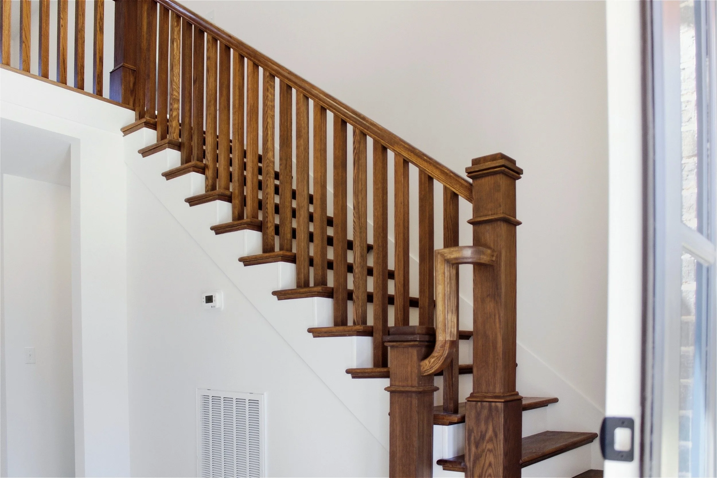 Wood staircase with wooden banister and balusters inside a house, with a wall and window on the right side.