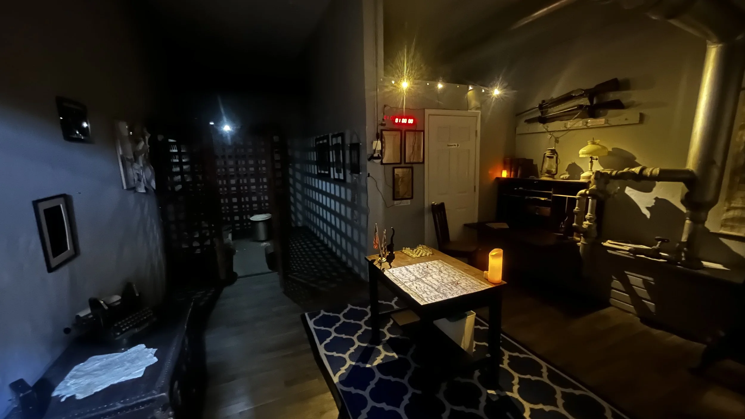 Dimly lit room with a table, a candle, a lamp, a cabinet, and various items on the walls and shelves, with some objects casting shadows.