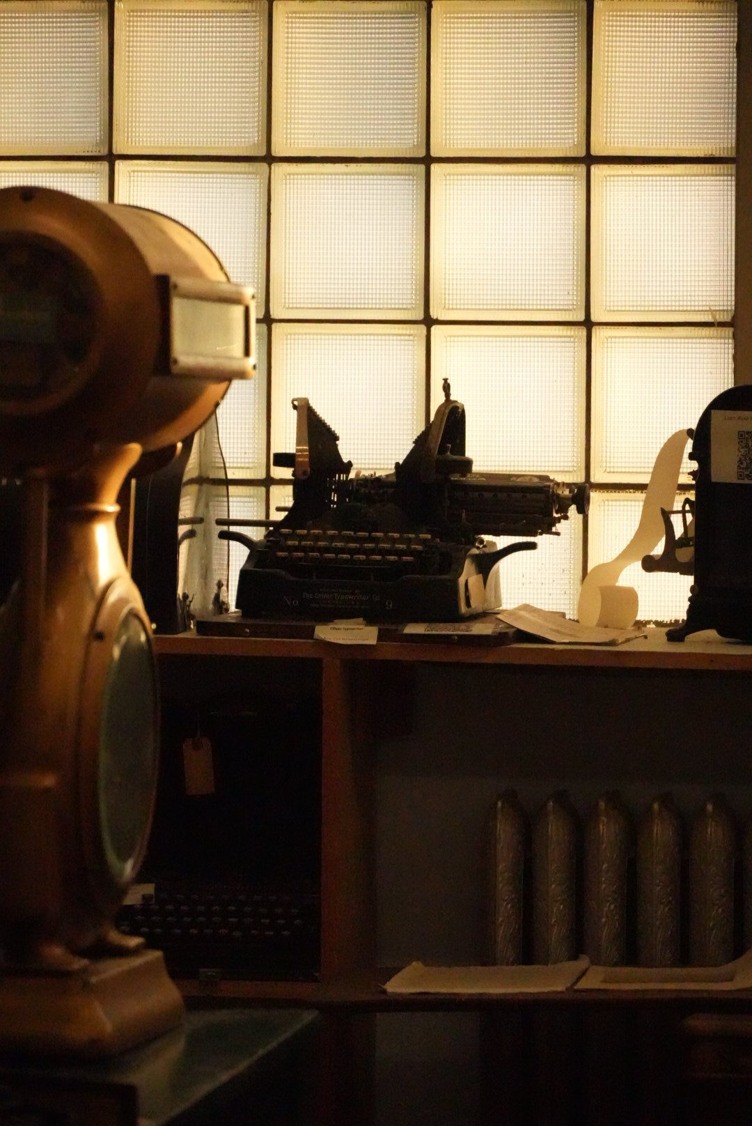 Vintage typewriter on a wooden desk, with a large glass block window in the background, and an antique telephone in the foreground.