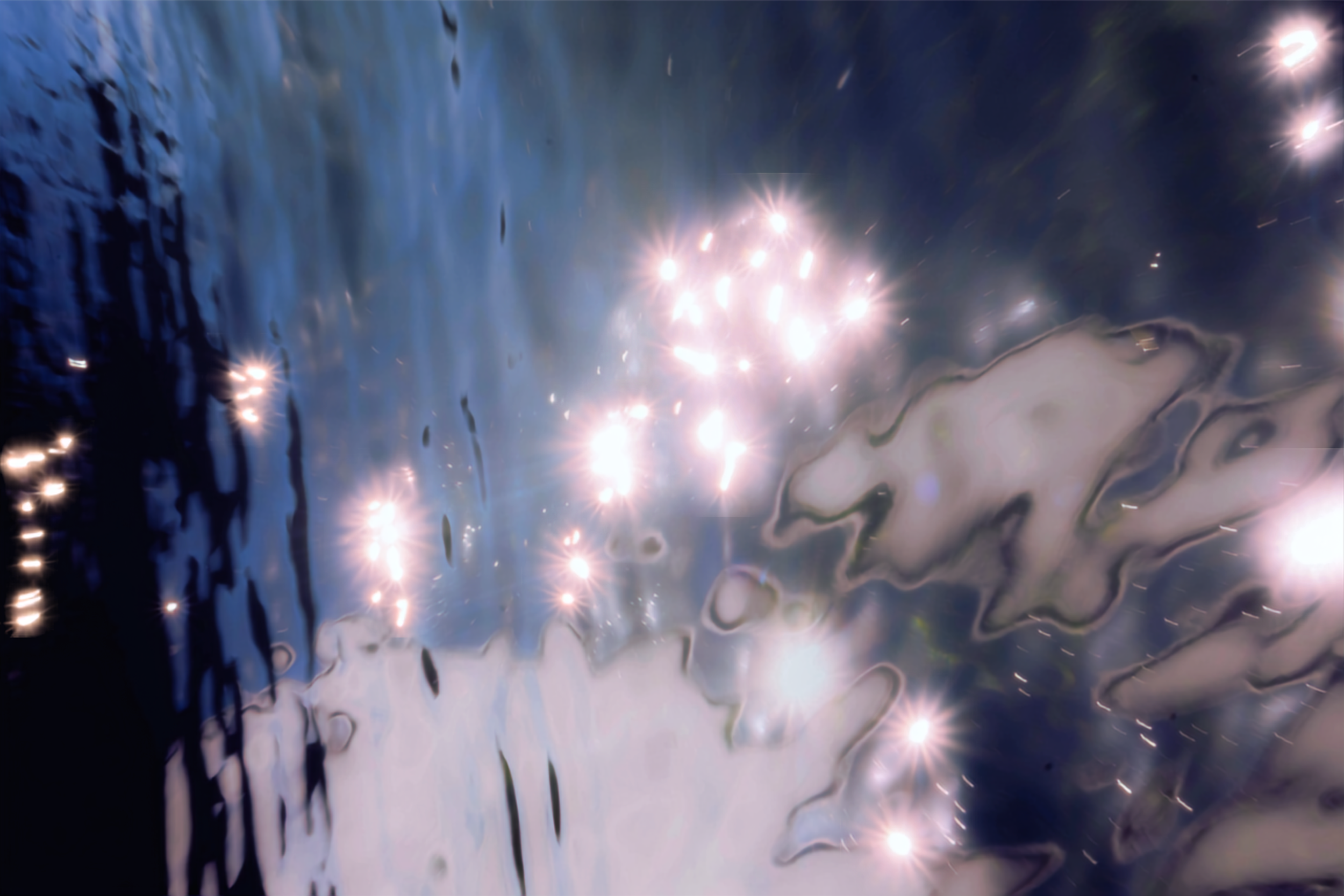 Close-up of water with light reflections and ripples, creating an abstract pattern with shiny spots and swirling textures.
