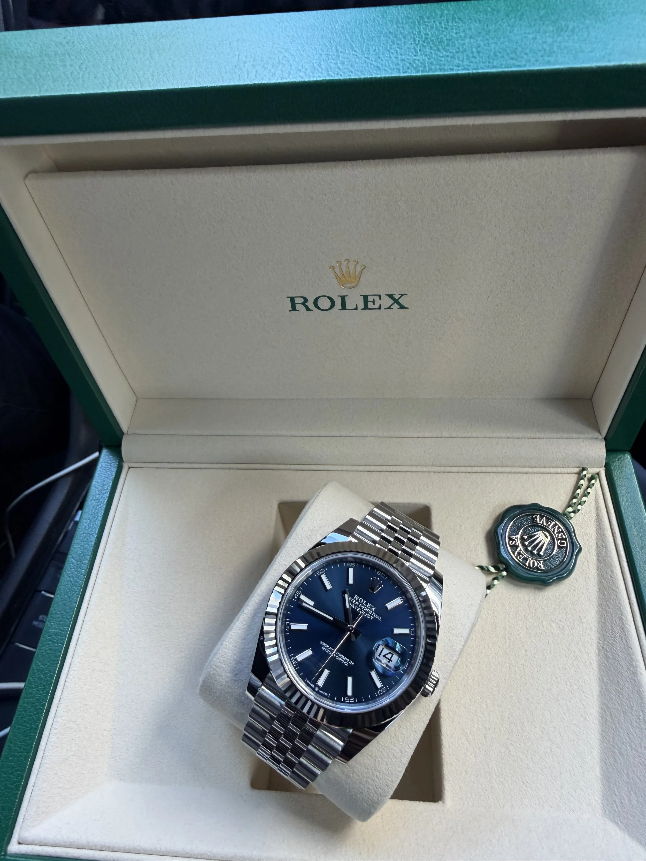 Ein Rolex-Uhr in einer grünen und weißen Box, mit einem blauen Zifferblatt und einem silbernen Metallarmband.