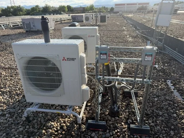 HVAC units and electrical equipment installed on a rooftop with gravel surface, and a fence in the background.