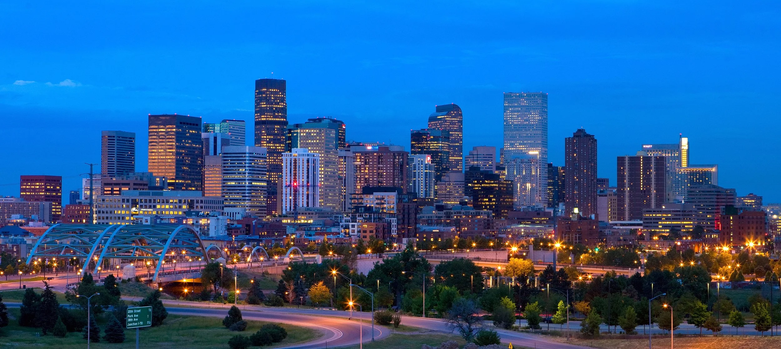 Nighttime cityscape of Denver skyline with illuminated skyscrapers and skyline park entrance in the foreground.