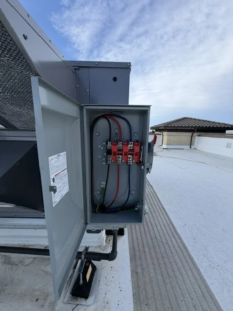Open electrical panel with red and black wires on a rooftop