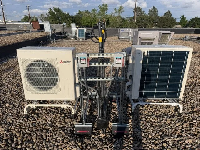HVAC or refrigeration system on a rooftop with two large units, electrical connections, and a backhoe in the background.