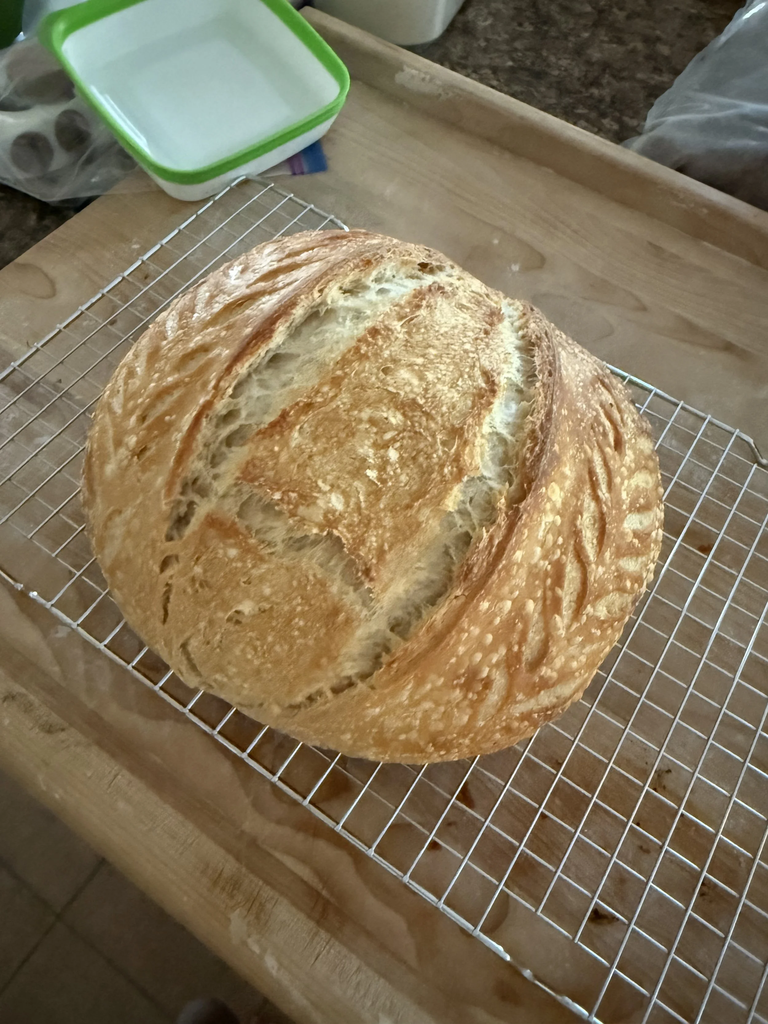 A freshly baked loaf of bread with a golden crust resting on a cooling rack on a wooden table.