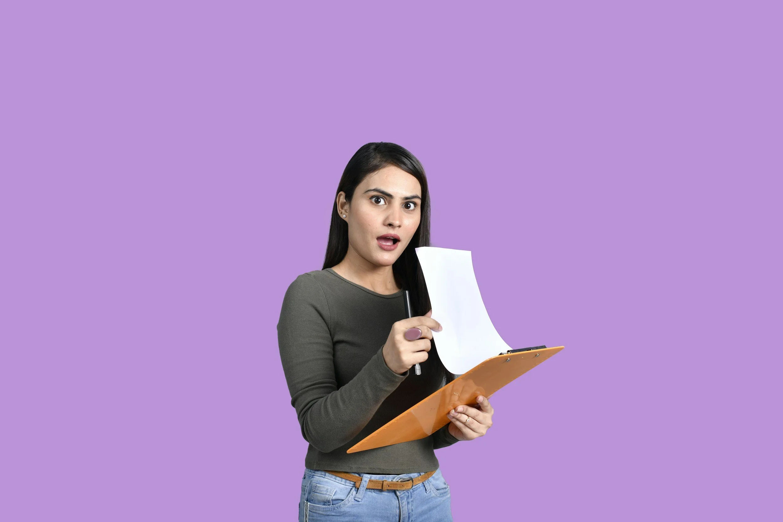 A surprised woman with long dark hair, holding a sheet of paper and a clipboard, standing against a purple background.