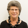 Grey haired woman with large black beaded necklace.