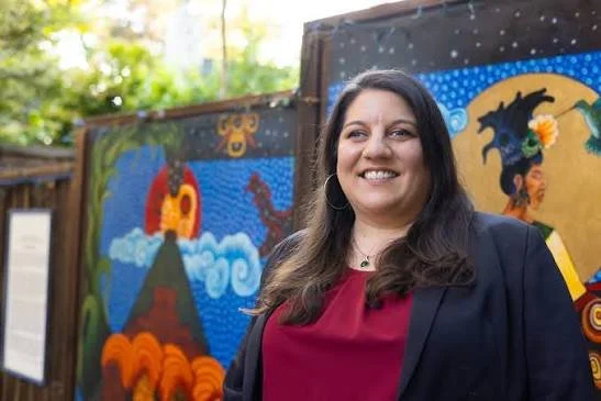 A brunette woman with a red top and blue blazer