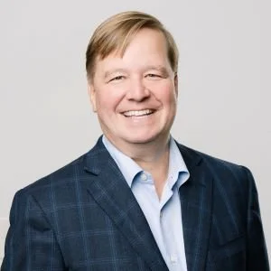 Man in a dark suit, with blonde hair and a smile