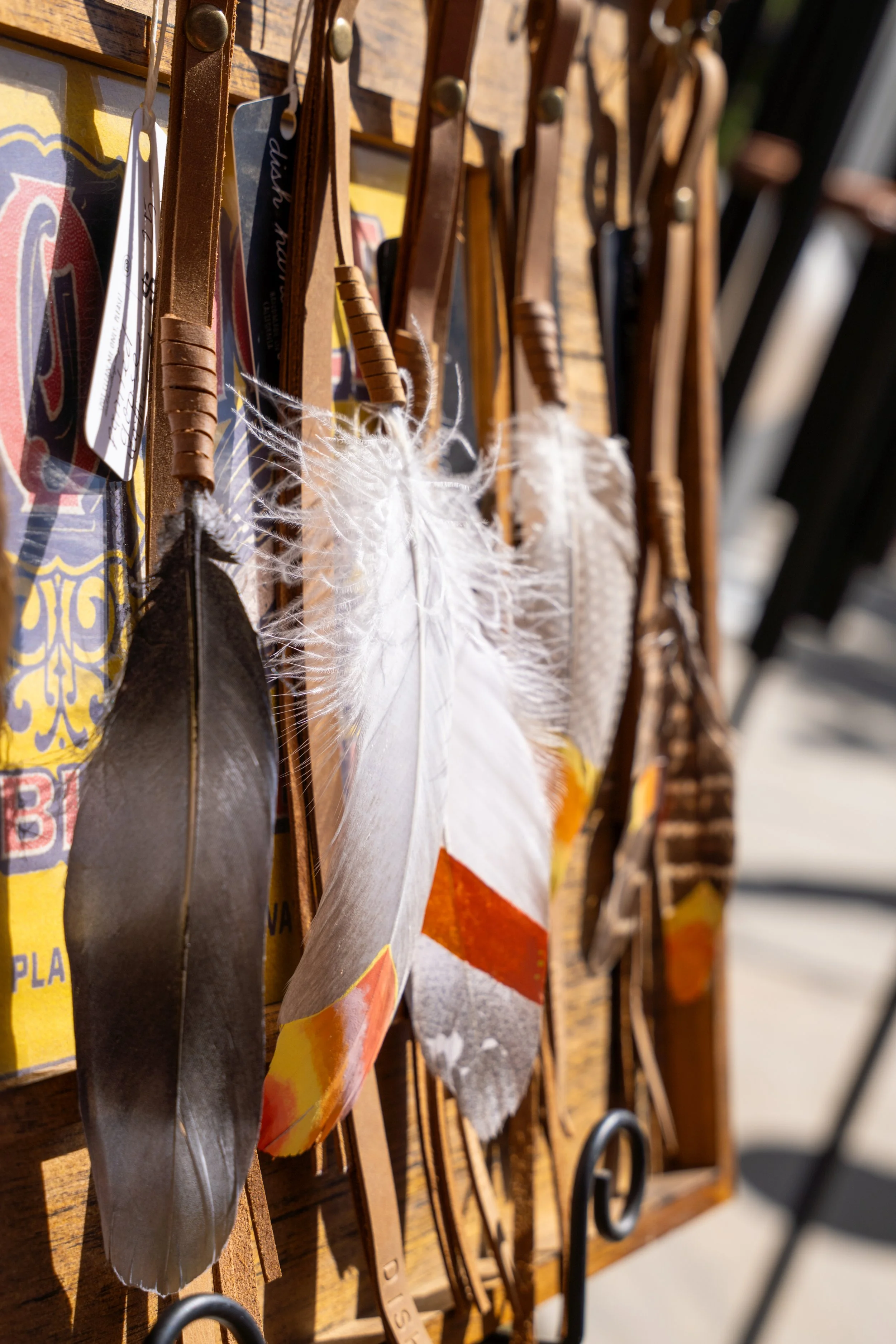 A close-up of various leather and feather paddles hanging on a wooden rack, with some tags attached.