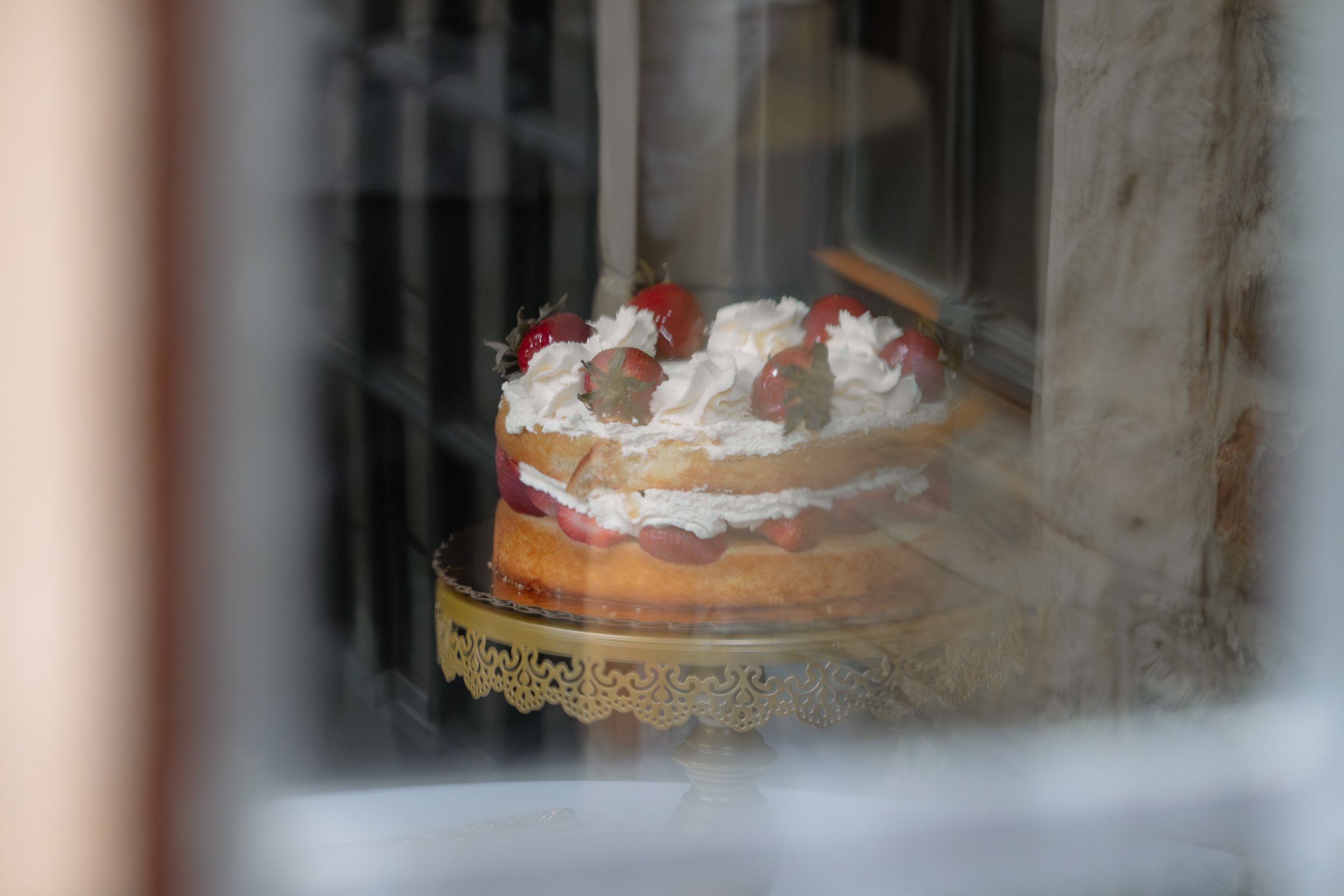 Cake with whipped cream and strawberries, viewed through a glass display case.