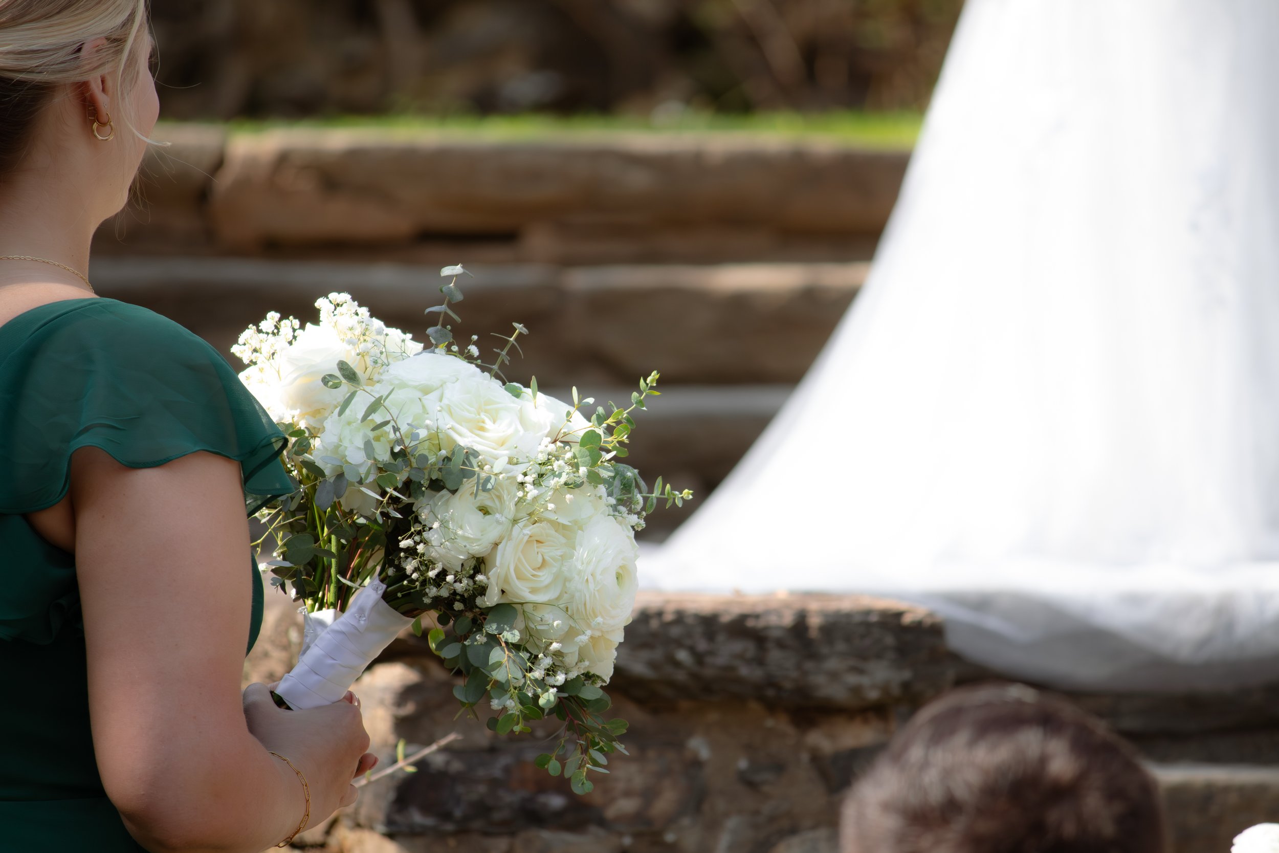 A woman holding a bouquet of white flowers during an outdoor wedding ceremony.
