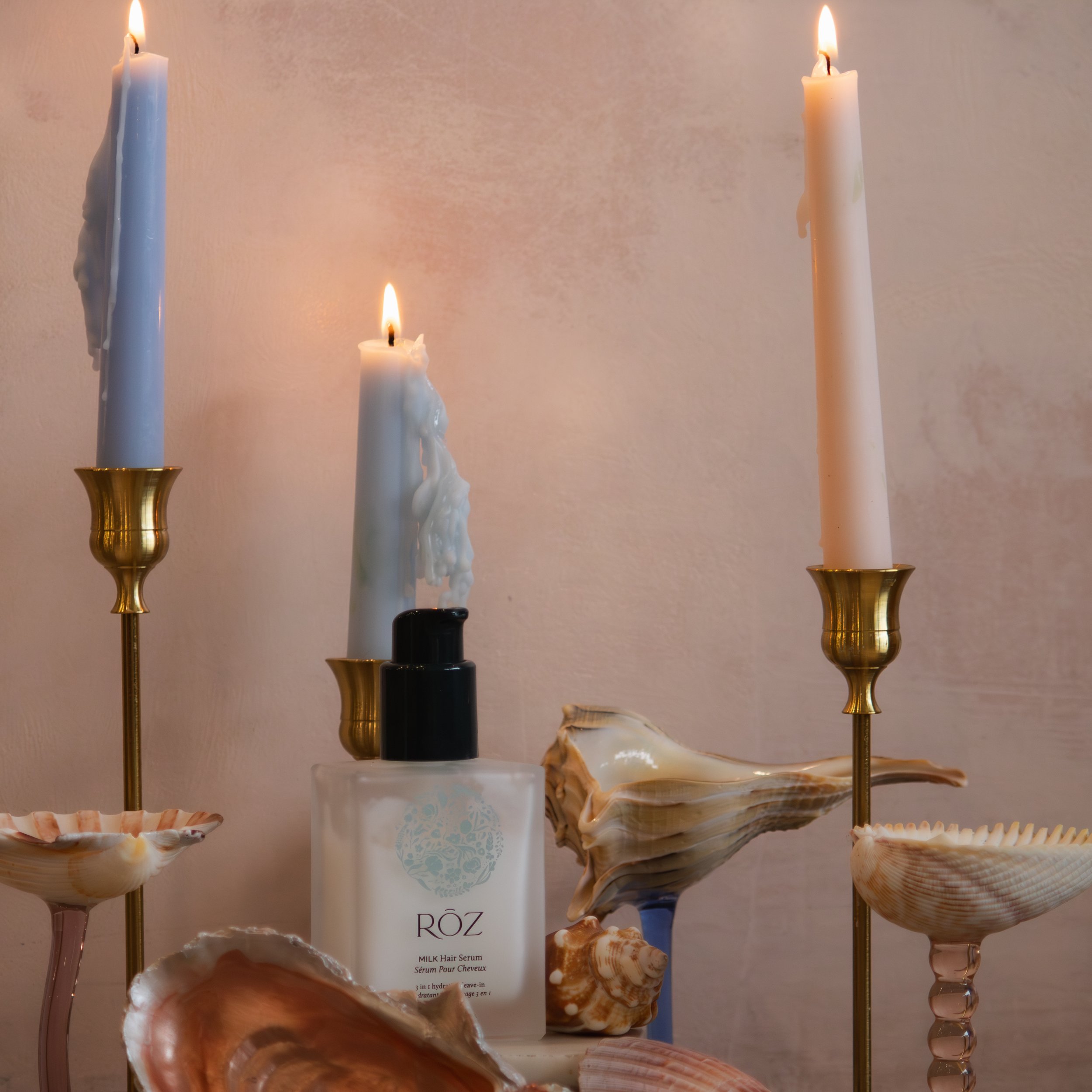 Several candles of different sizes and colors with lit flames, placed on shells and stands, with a white background and some text in the lower part of the image.