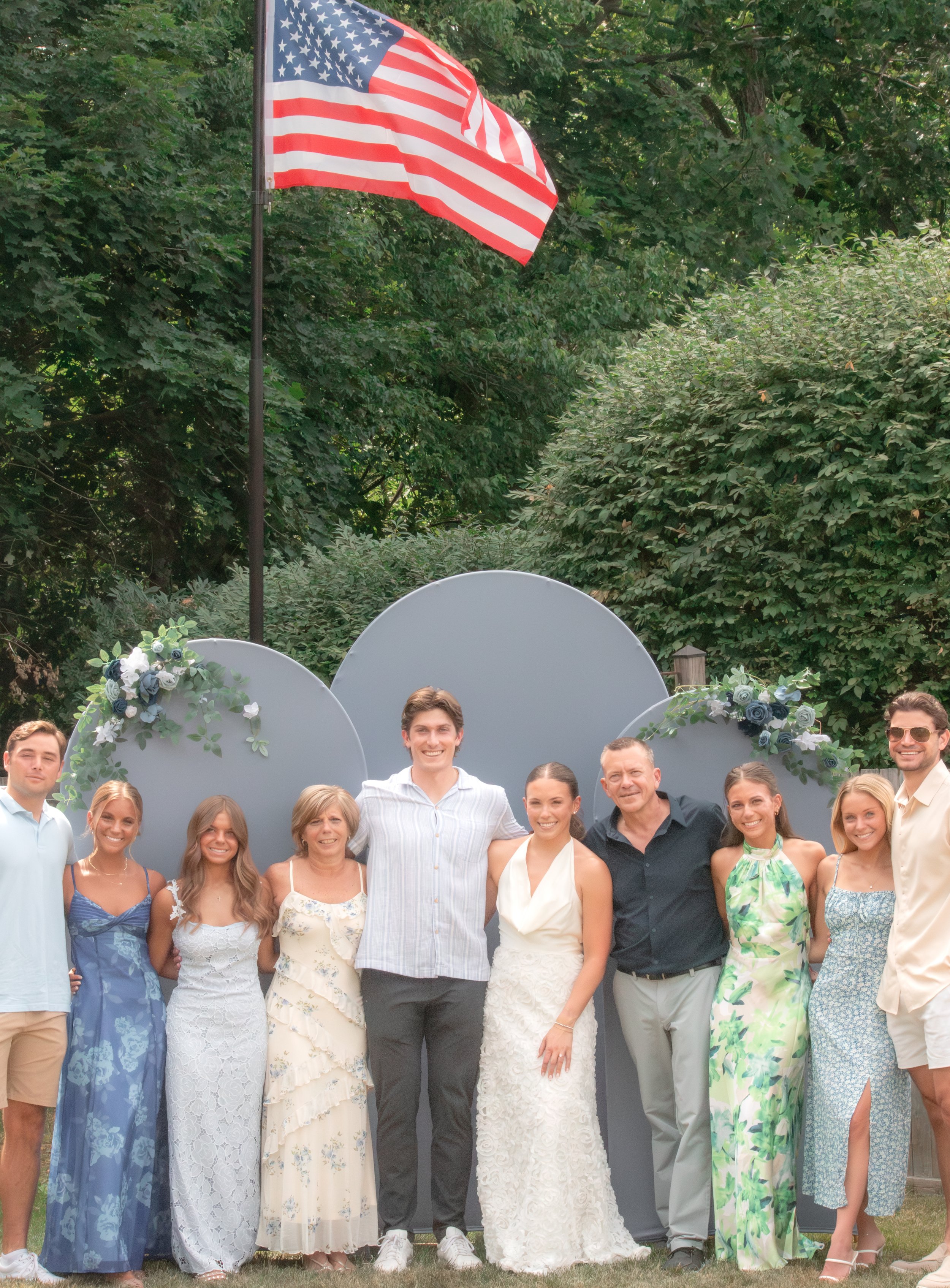 A group of people gathered outdoors for a celebration, with American flag and decorative balloons in the background.