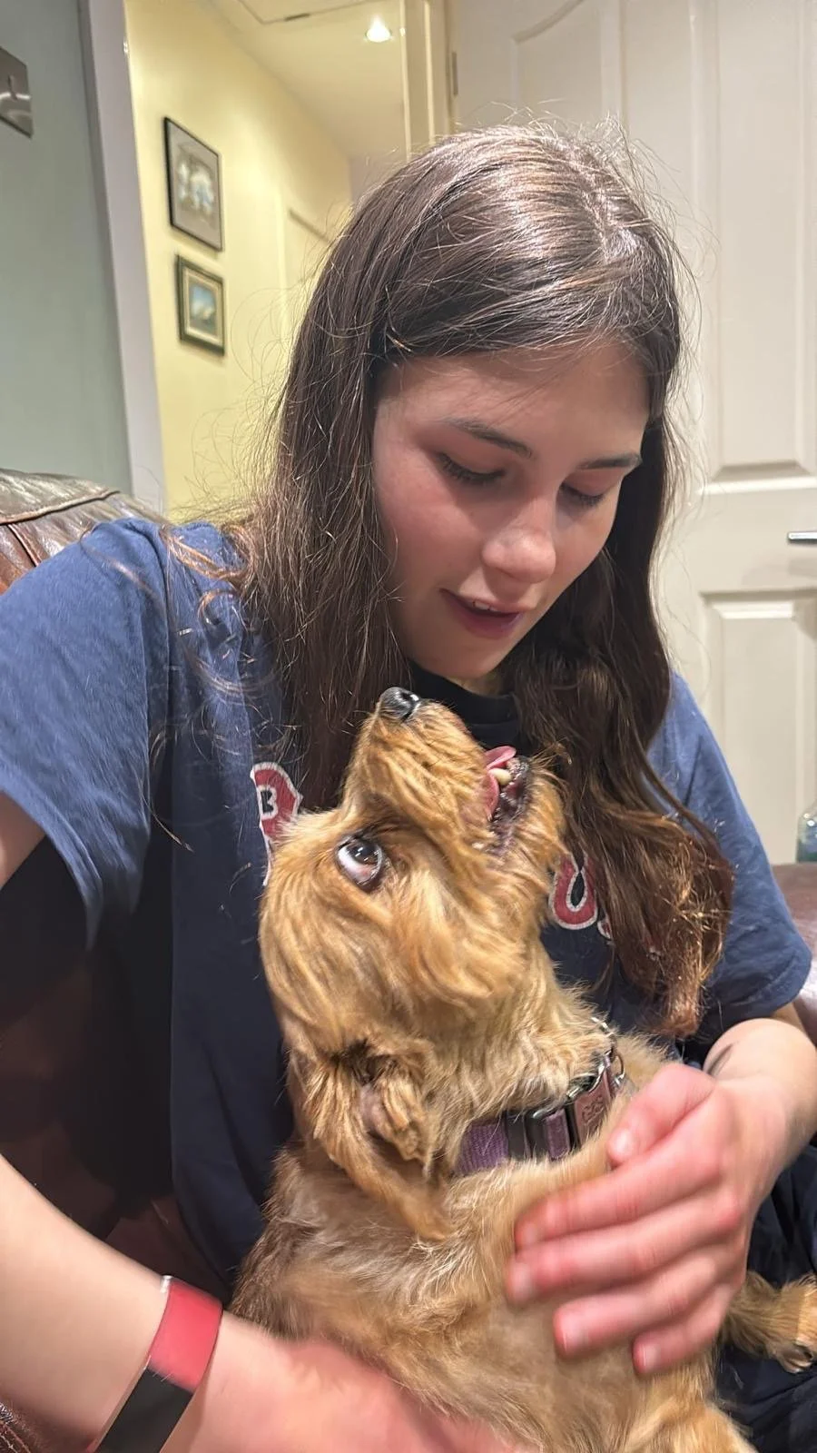 A young woman with long brown hair holding a small brown dog during playtime indoors.