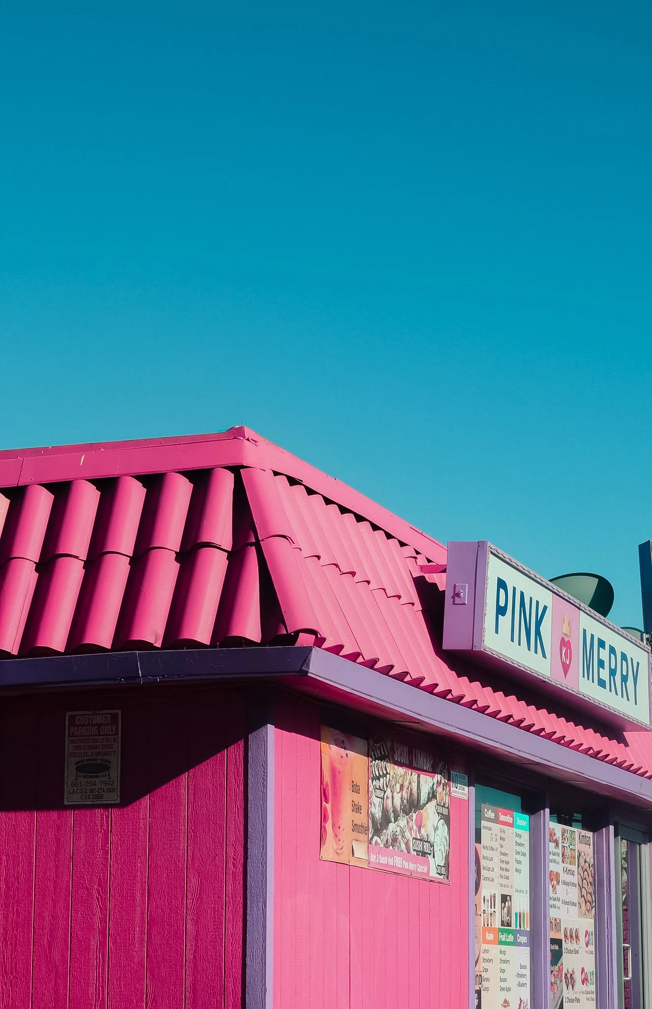 Pink storefront with a pink tiled roof and colorful posters displaying menu items.
