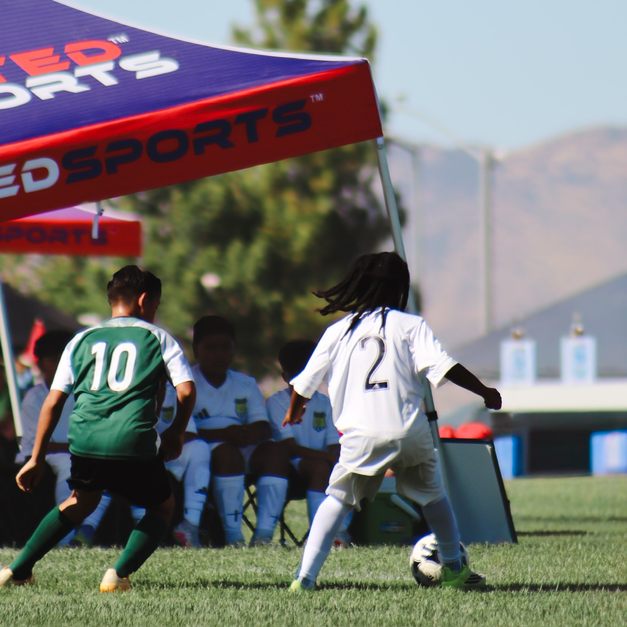 A group of young soccer players, wearing jerseys with numbers, are lined up in a formation on a grassy field, preparing to kick a soccer ball during a game or practice.
