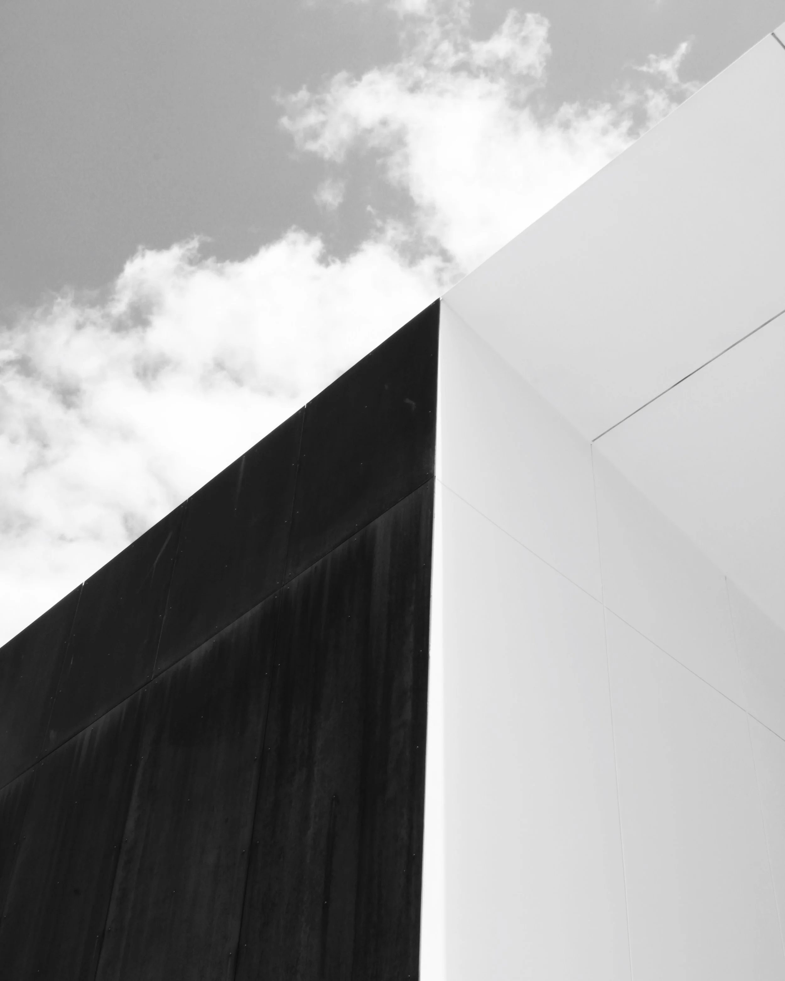 Black and white geometric structure with a dark black section on the lower left and a white section on the upper right, against a background of a partly cloudy sky.