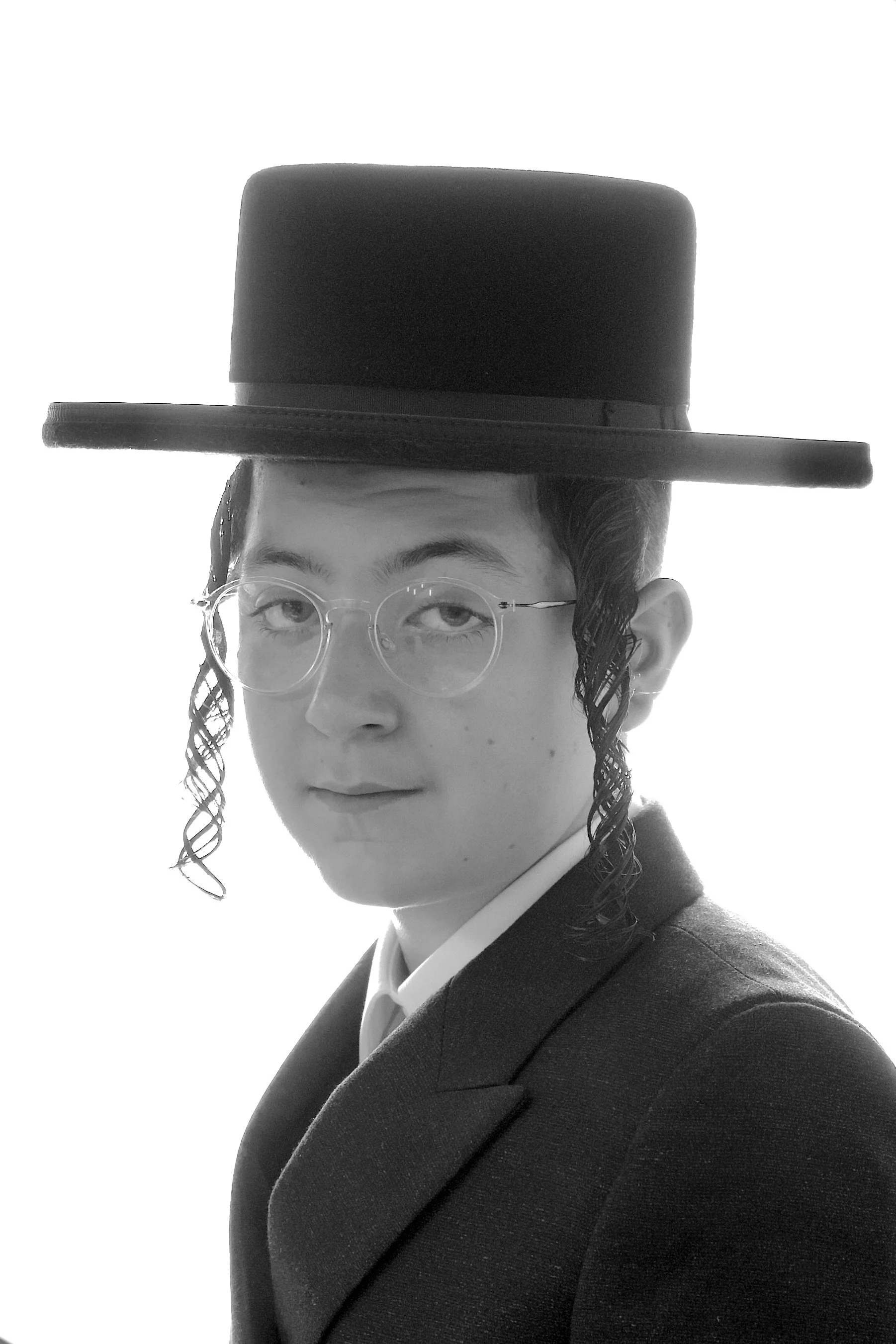 Black and white photo of a person wearing glasses, a suit, and a wide-brimmed hat, looking towards the camera with a serious expression.