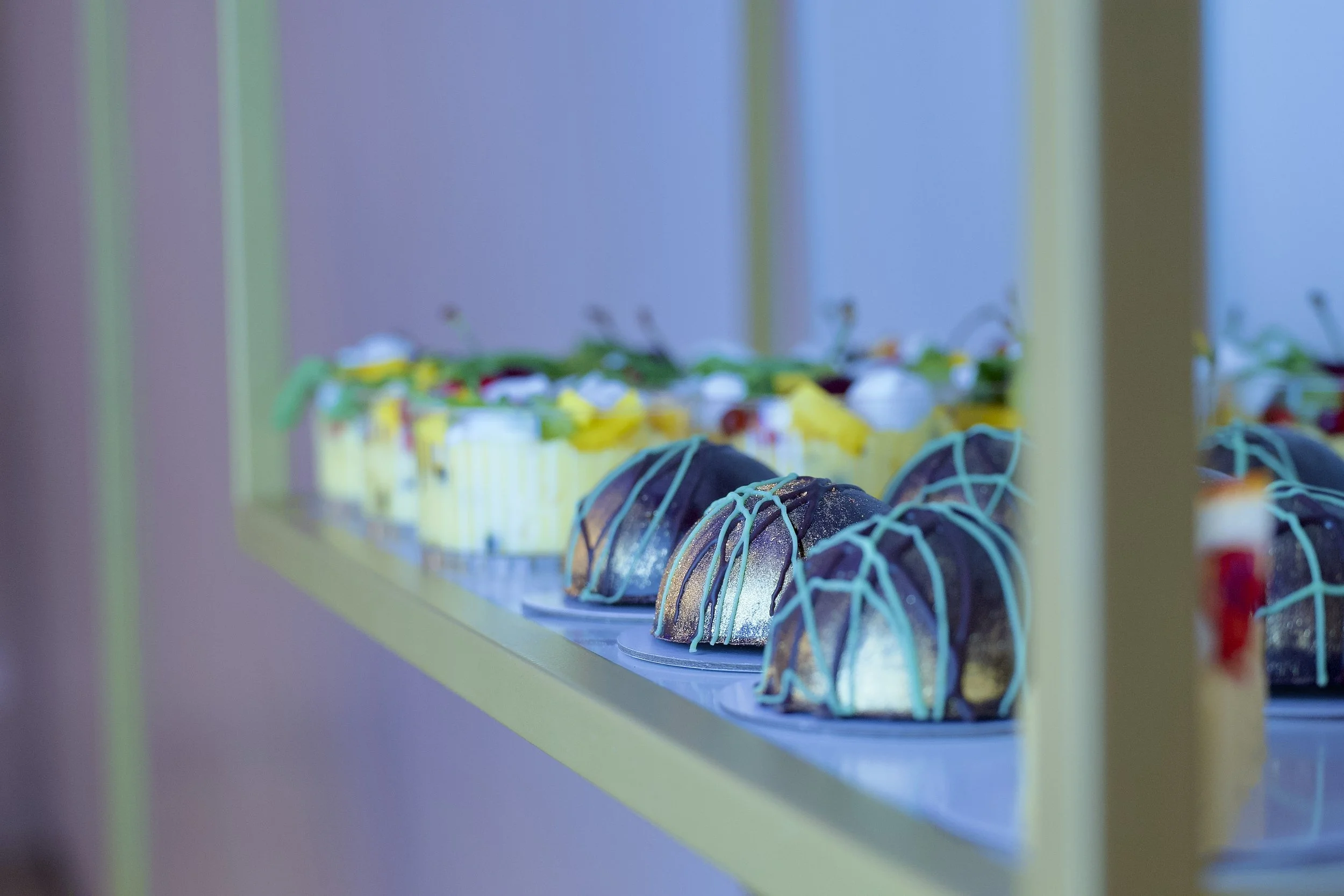 Colorful decorated cupcakes with blue icing and sprinkles, displayed on a yellow shelf.