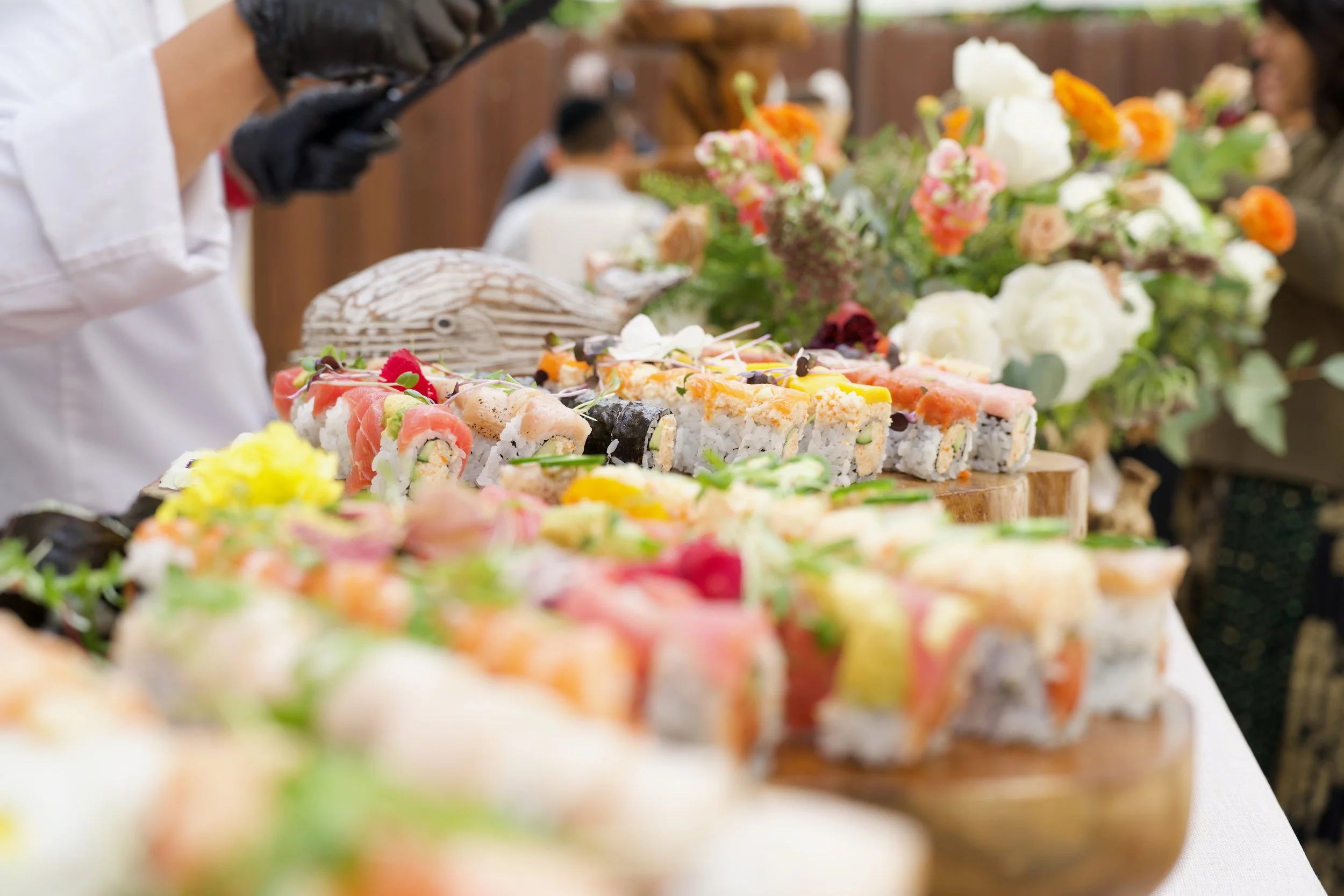 A display of assorted sushi rolls with various ingredients, accompanied by a floral arrangement, at a social gathering.