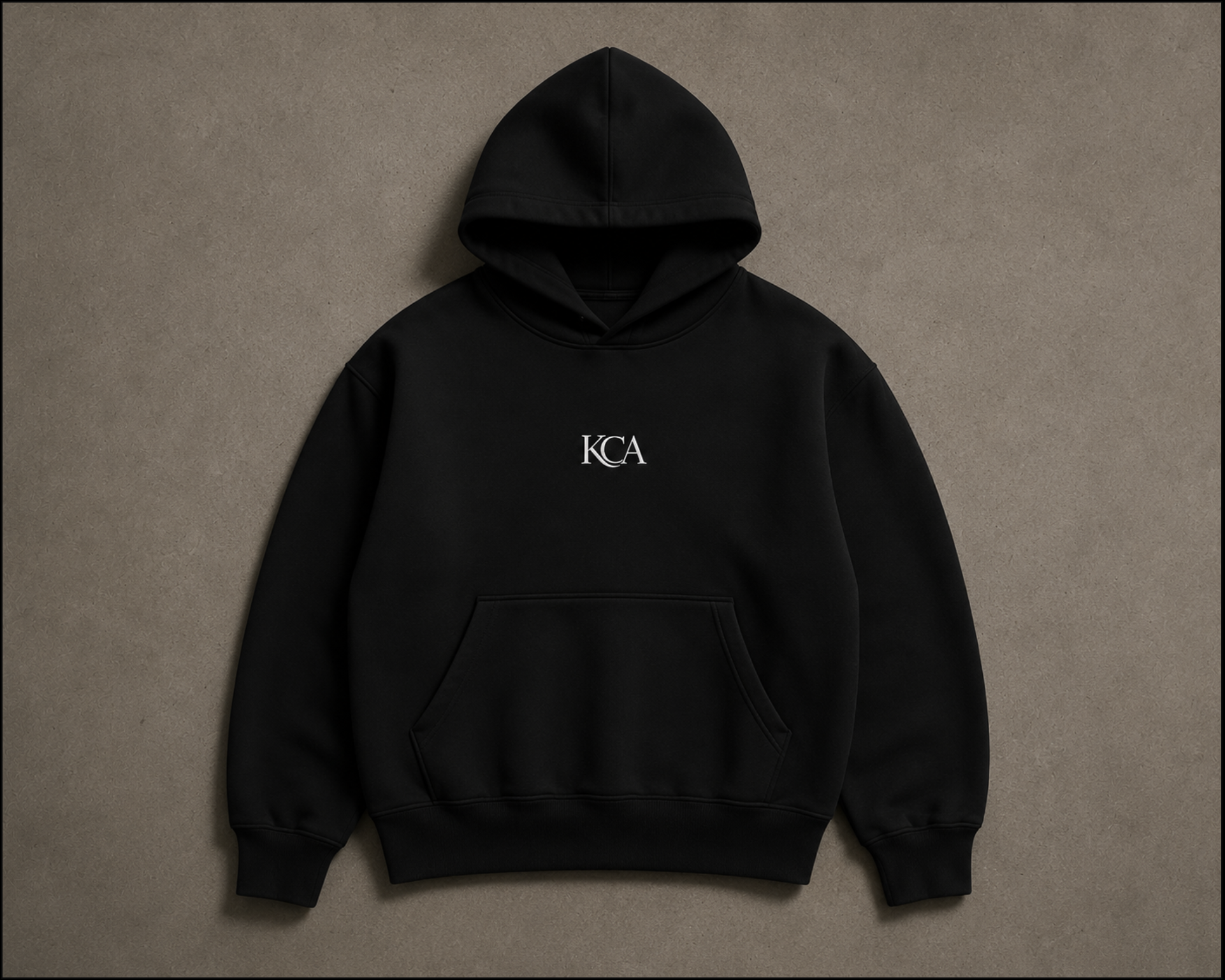 Black hoodie with 'KCA' embroidered on the chest, laid flat on a beige background.
