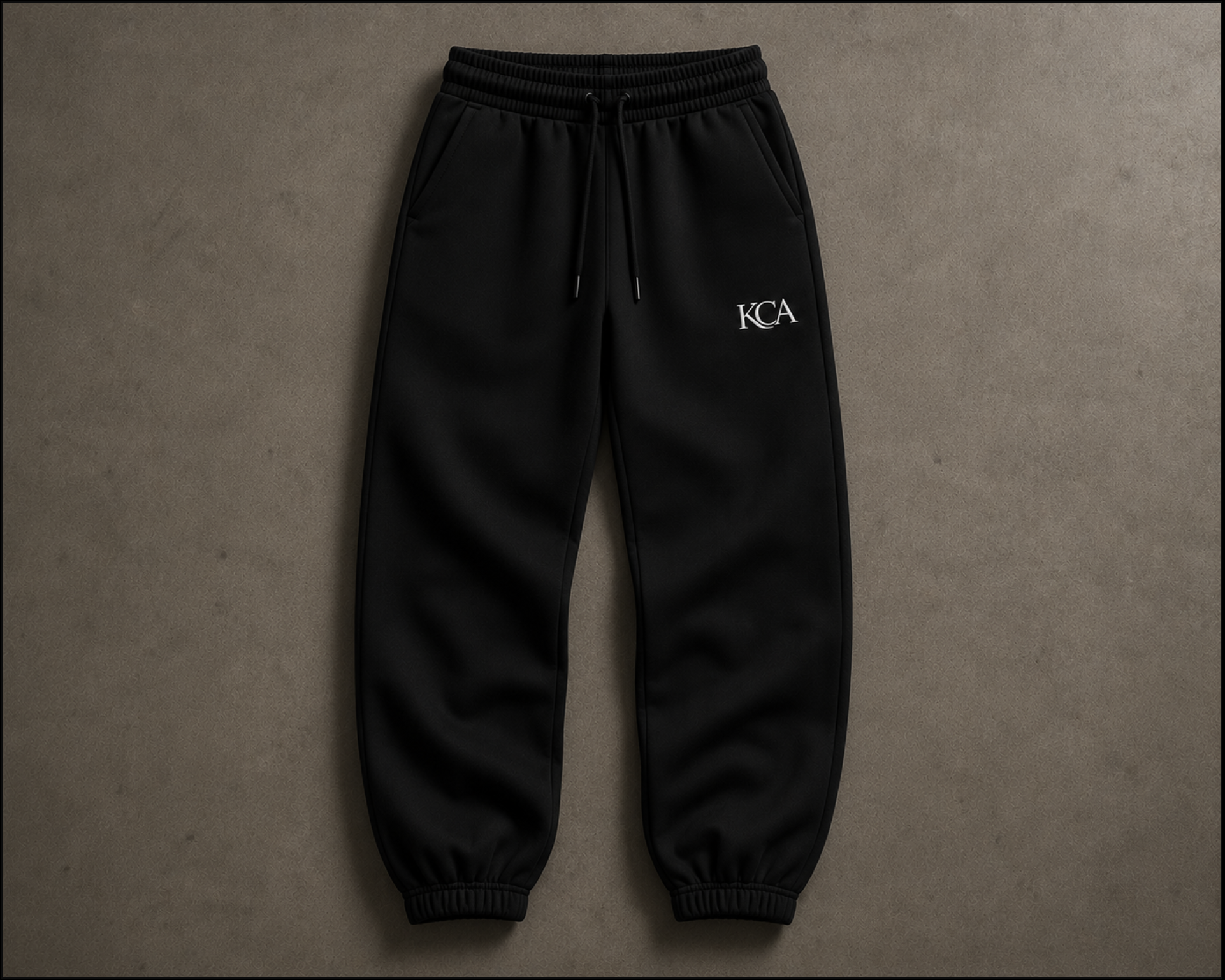 Black sweatpants with an elastic waistband, drawstring, and cuffs, featuring a white 'KCA' logo on the upper left thigh.