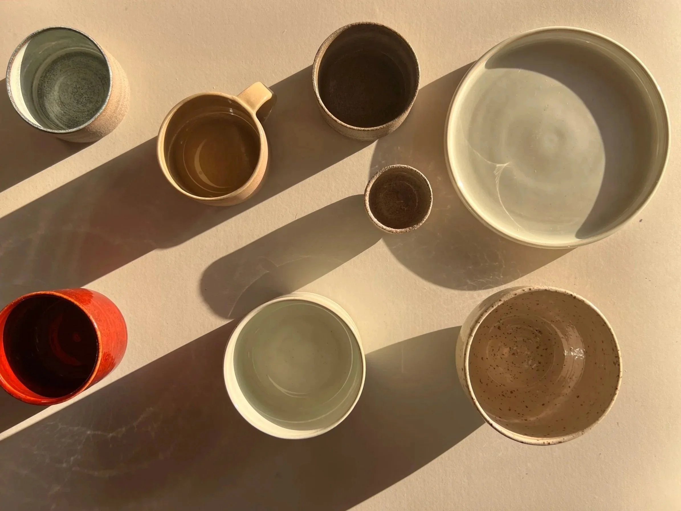 Six ceramic cups or bowls arranged on a light-colored surface, casting shadows in sunlight.