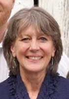 A woman with short gray hair, smiling, wearing a navy blue top, standing outdoors.