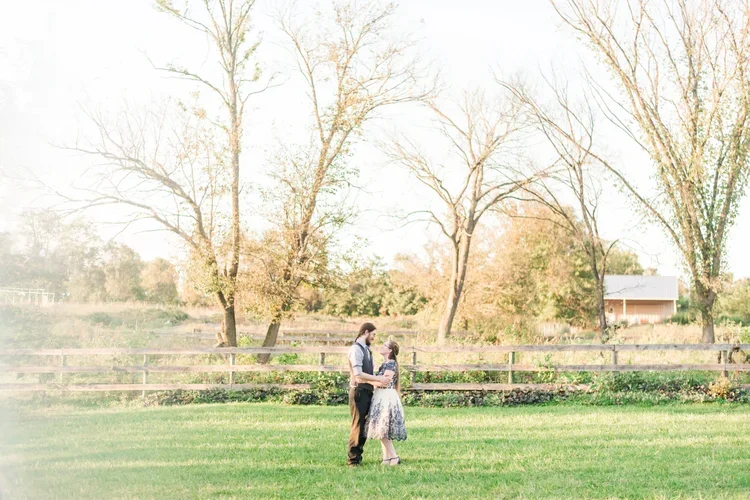 A couple dancing on a grassy field with trees and a fence in the background.