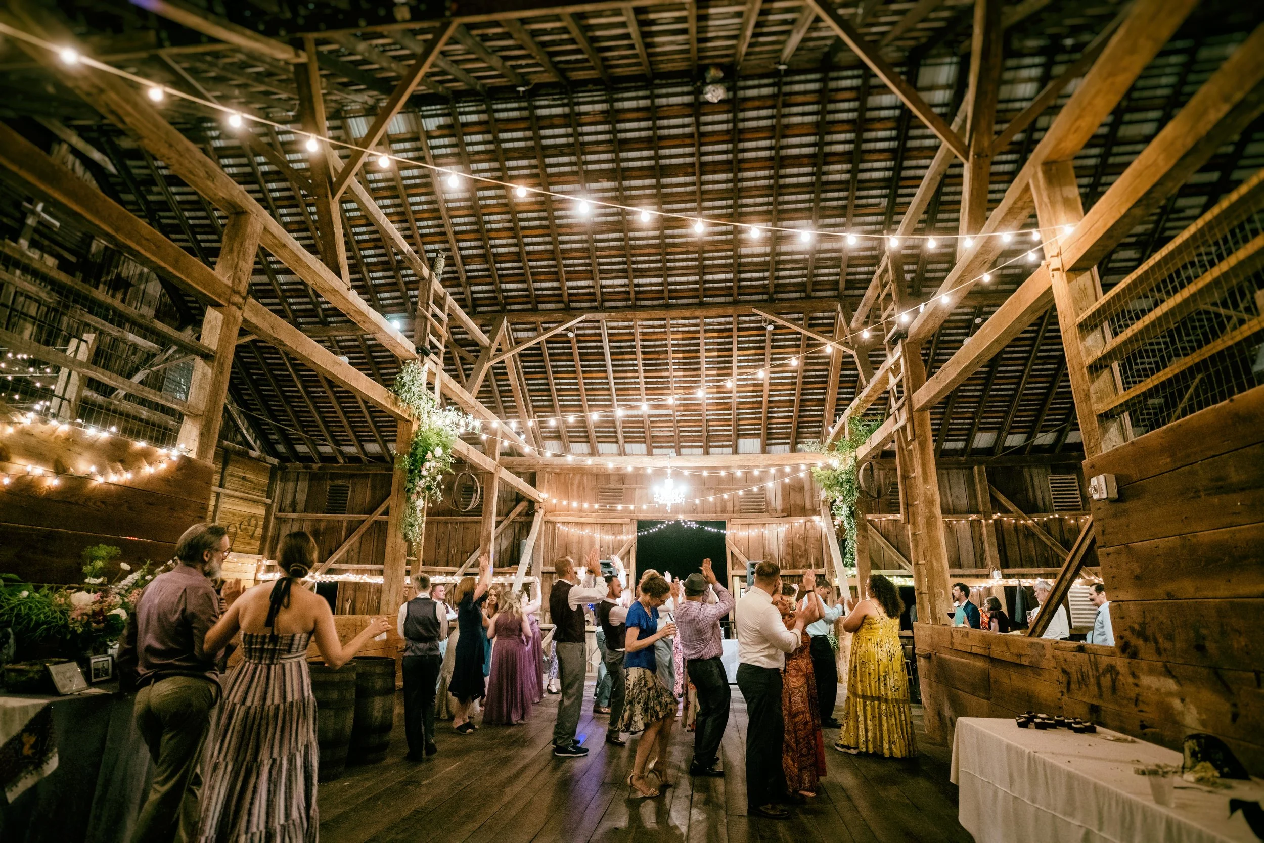 Guests dancing and socializing at a rustic barn wedding reception at Rocklands Farm Winery decorated with string lights and greenery.