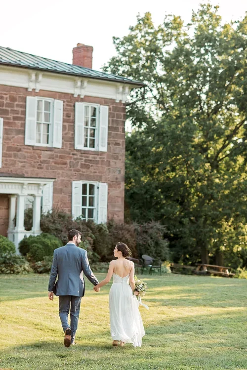 A bride and groom holding hands and walking on a grassy lawn at Rocklands Farm Winery