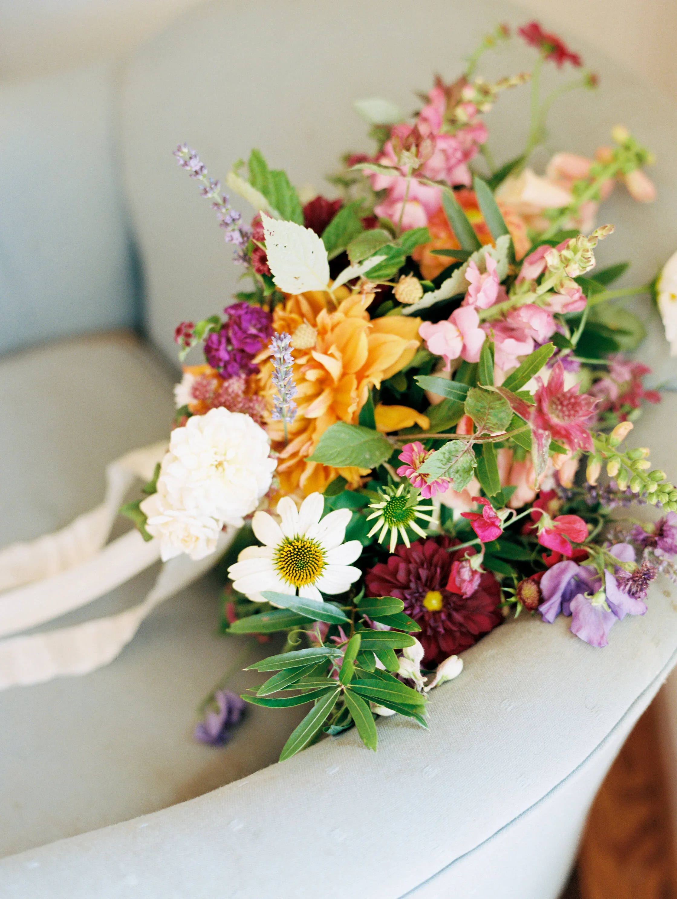 A colorful bouquet of flowers including white, purple, pink, orange, and green flowers and foliage, resting on a light-colored surface.