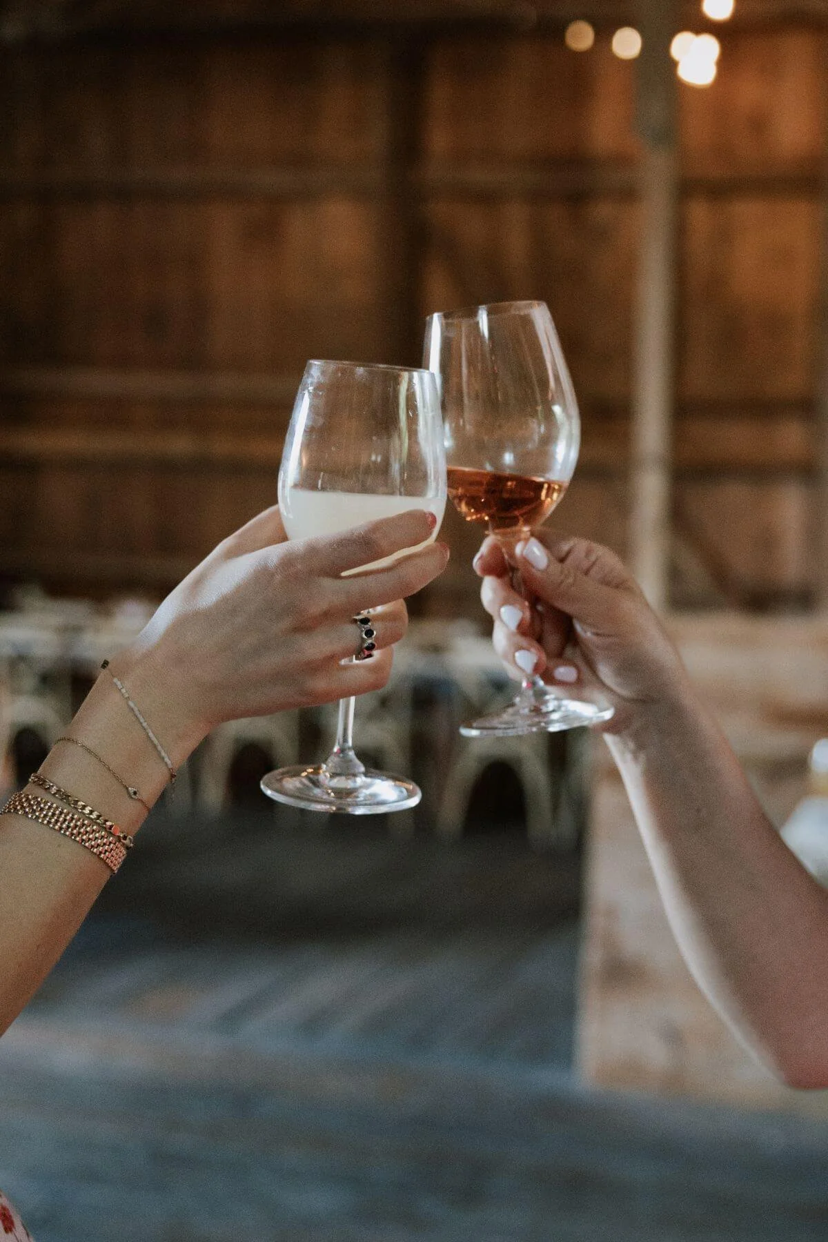 Two people toasting with glasses of white wine and rosé wine in a cozy, dimly lit setting.