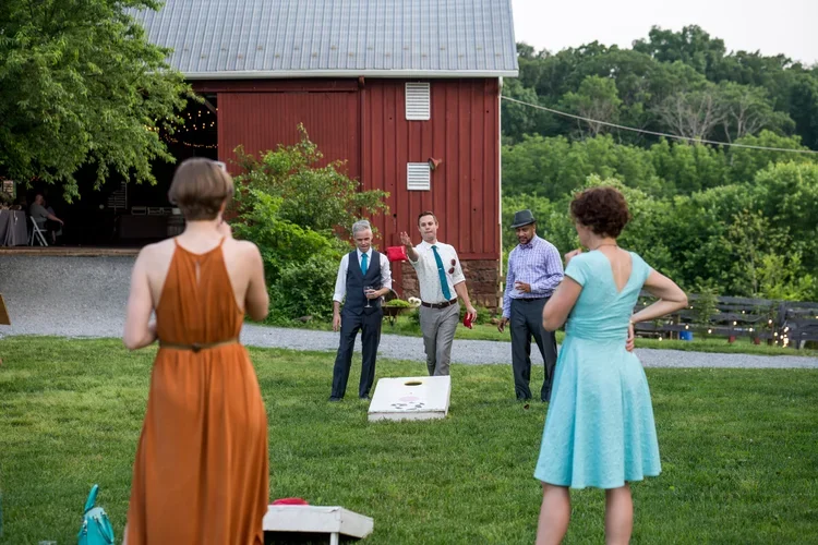 People playing cornhole outdoors in front of the Rocklands Farm Winery barn at a wedding