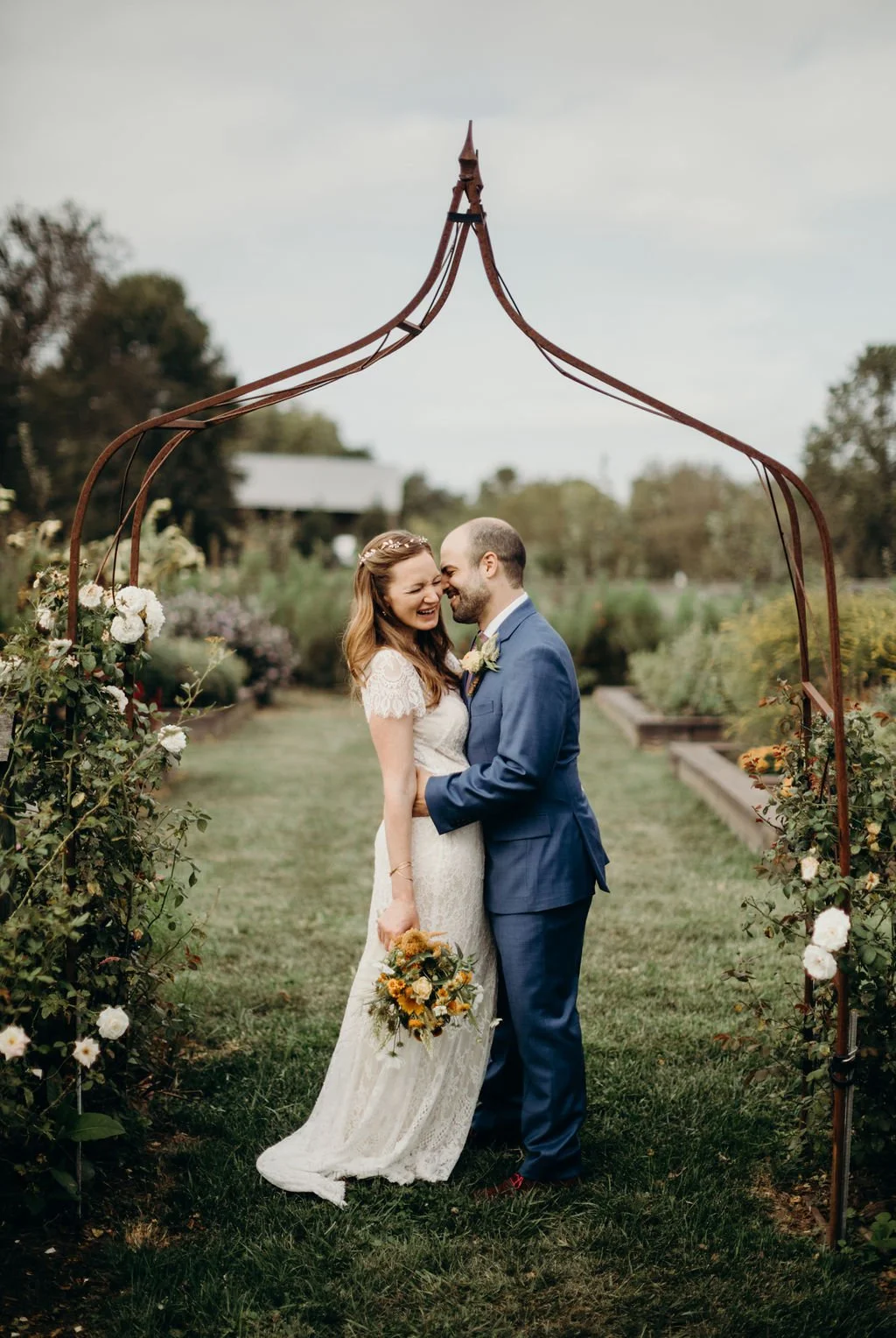 A bride and groom smiling and touching foreheads under a rustic metal archway during their outdoor wedding at Rocklands Farm Winery