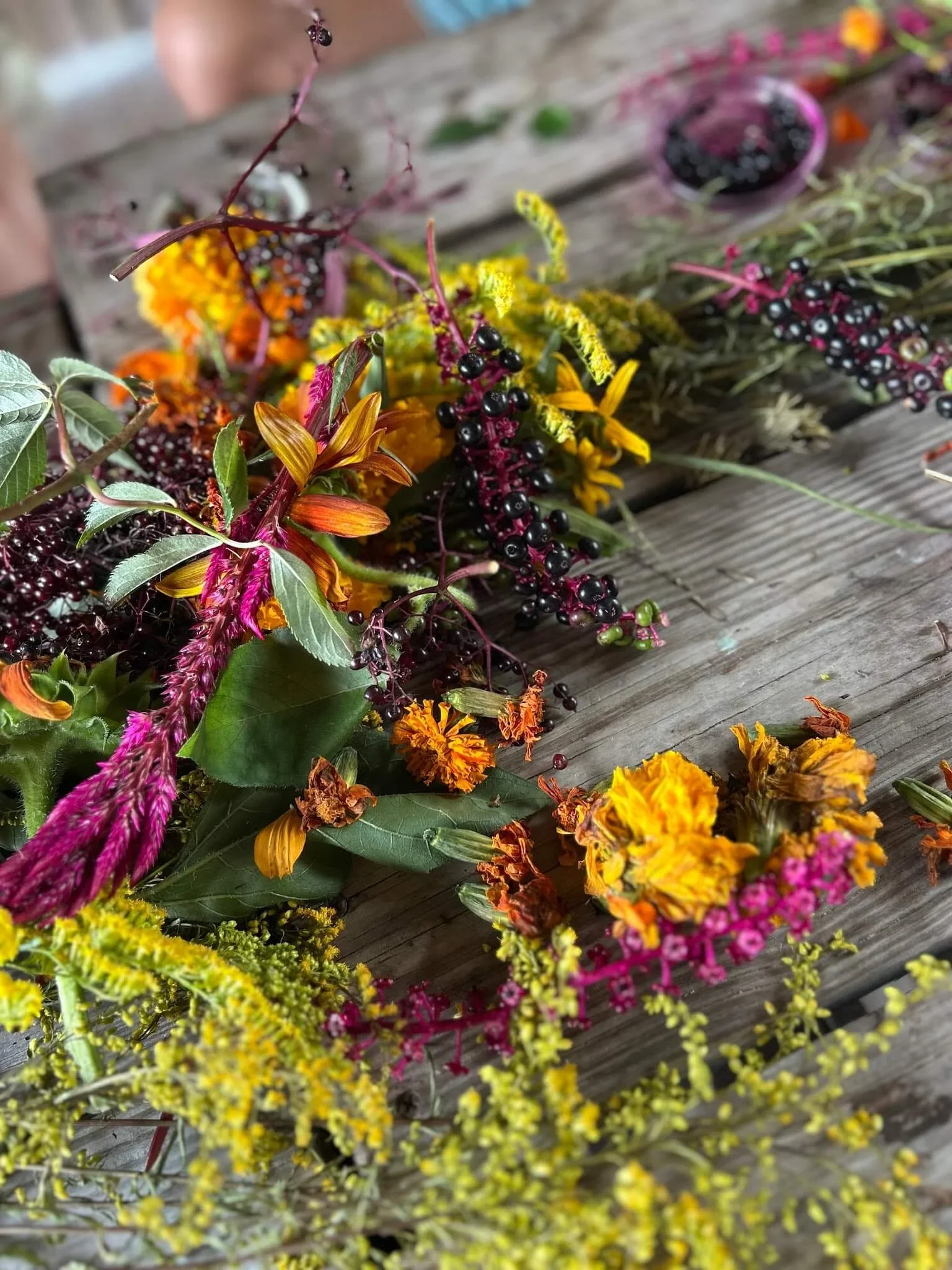Colorful floral and berry arrangement on a wooden surface, featuring yellow, orange, pink, and black elements.