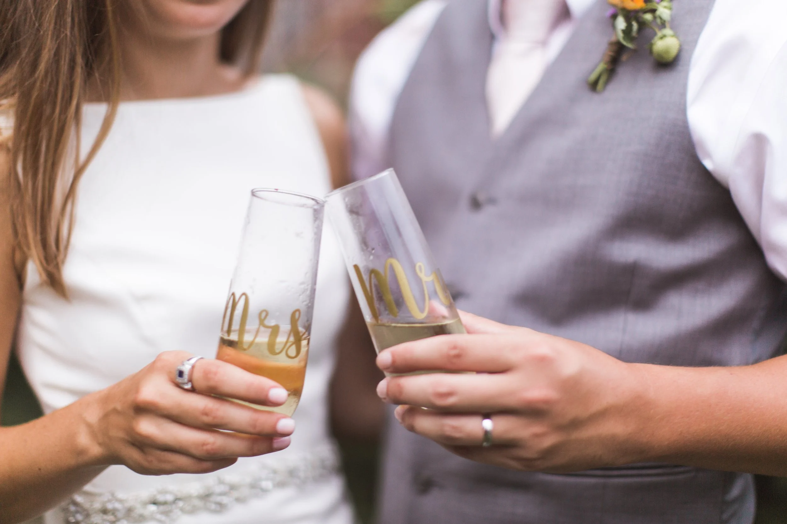 Two people dressed in wedding attire are holding champagne glasses and toasting at a celebration.